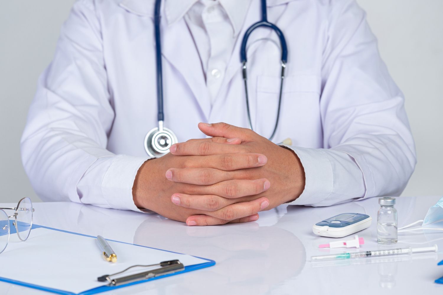 A doctor is sitting at a desk with his hands folded.