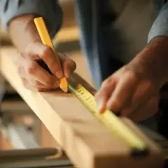 hands with tape measure and pencil marking cut line on a piece of wood