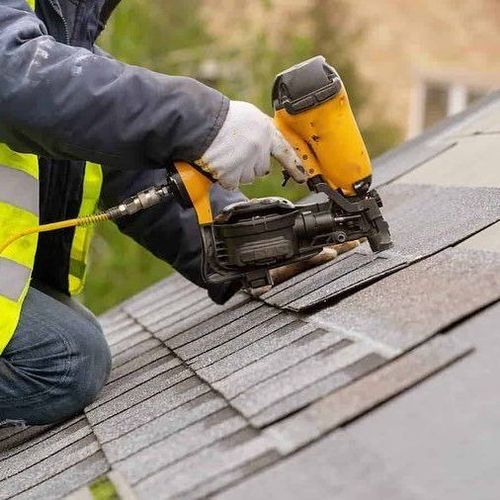 man holding a nail gun on a roof installing new shingles