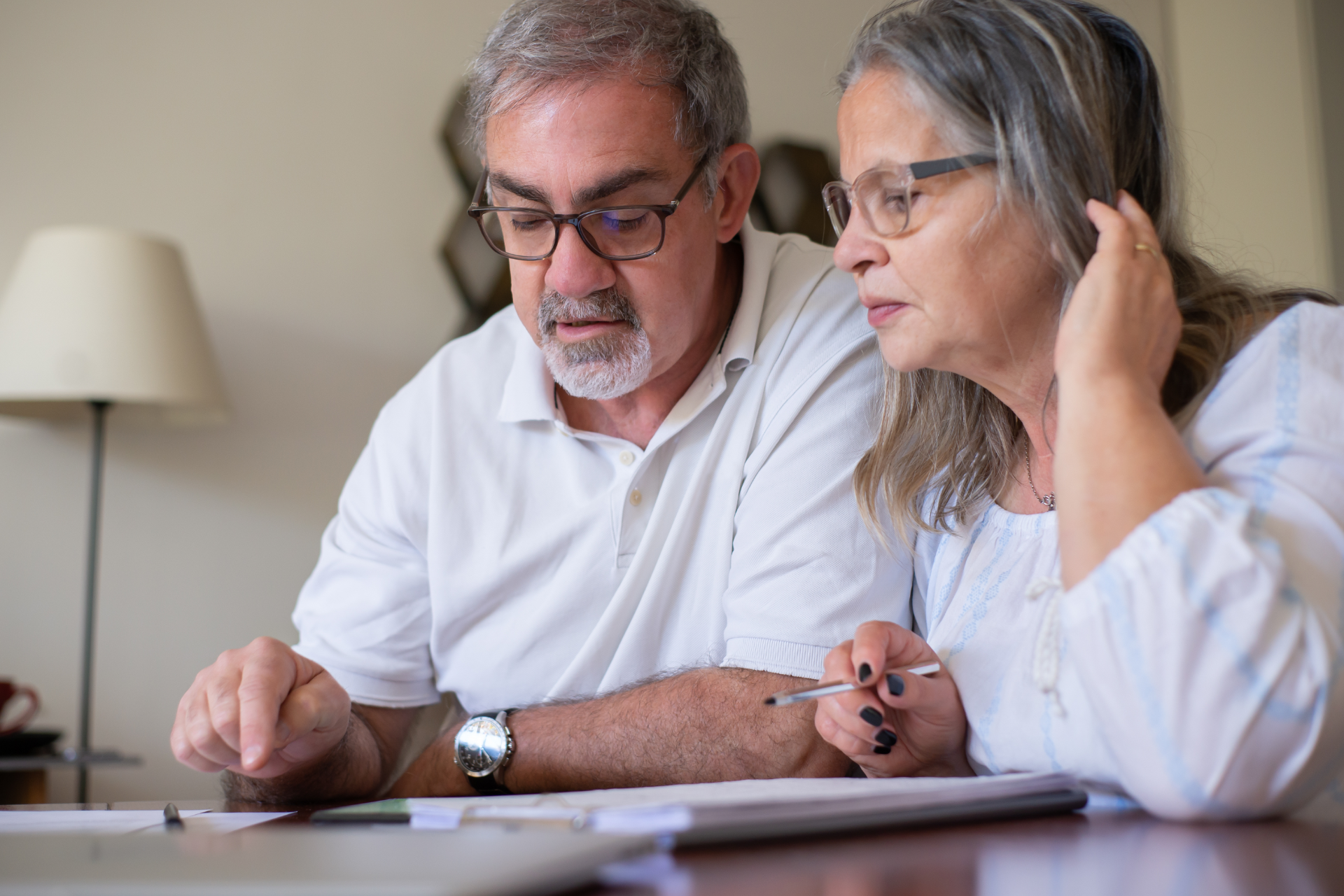 Older couple, wearing glasses, reviewing documents, looking concerned, indoors.
