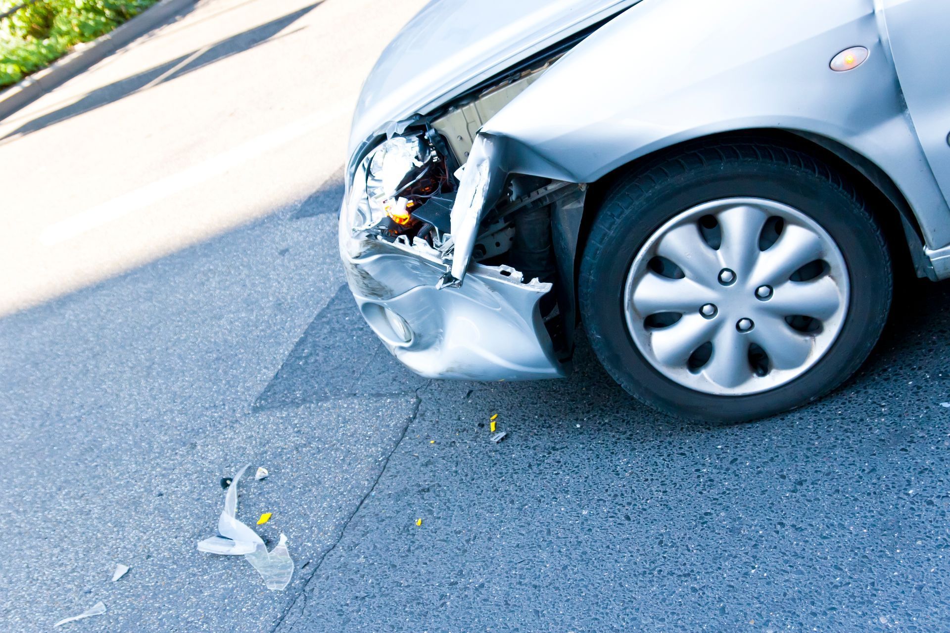 Silver car with front-end damage, debris on asphalt.