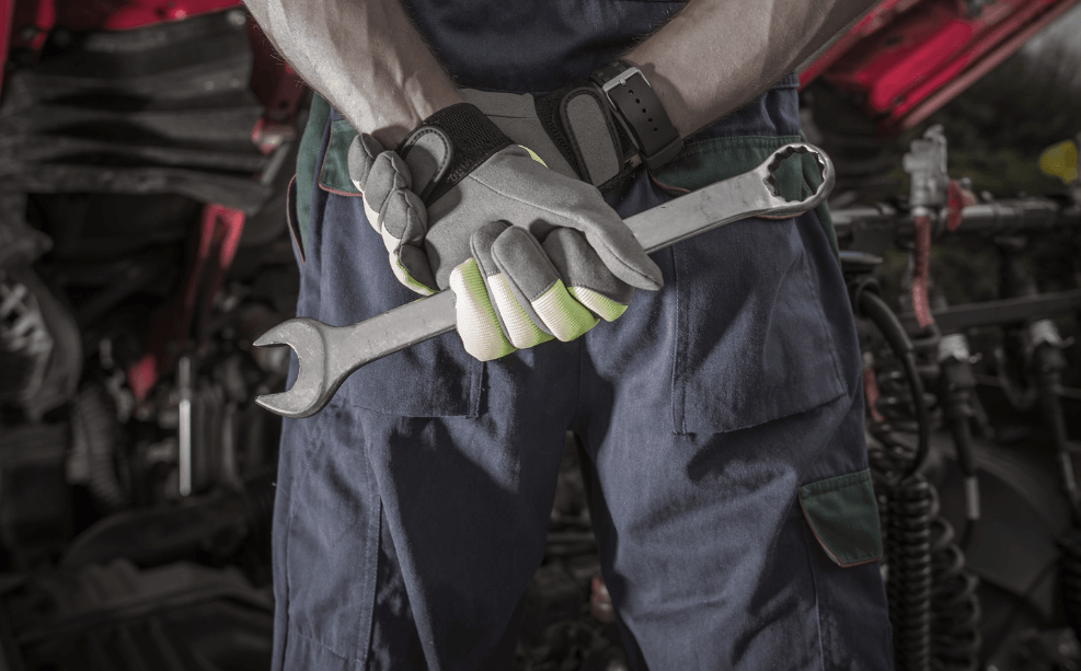 a mechanic holding a wrench in front of a car