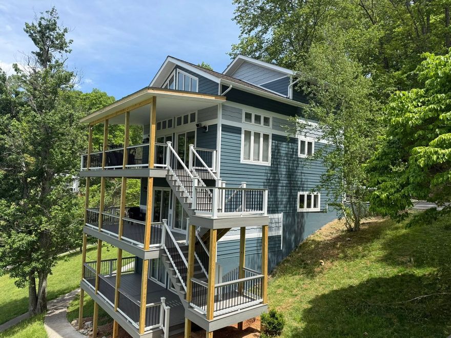 Blue house with wraparound porches and exterior stairs on a grassy hillside surrounded by trees
