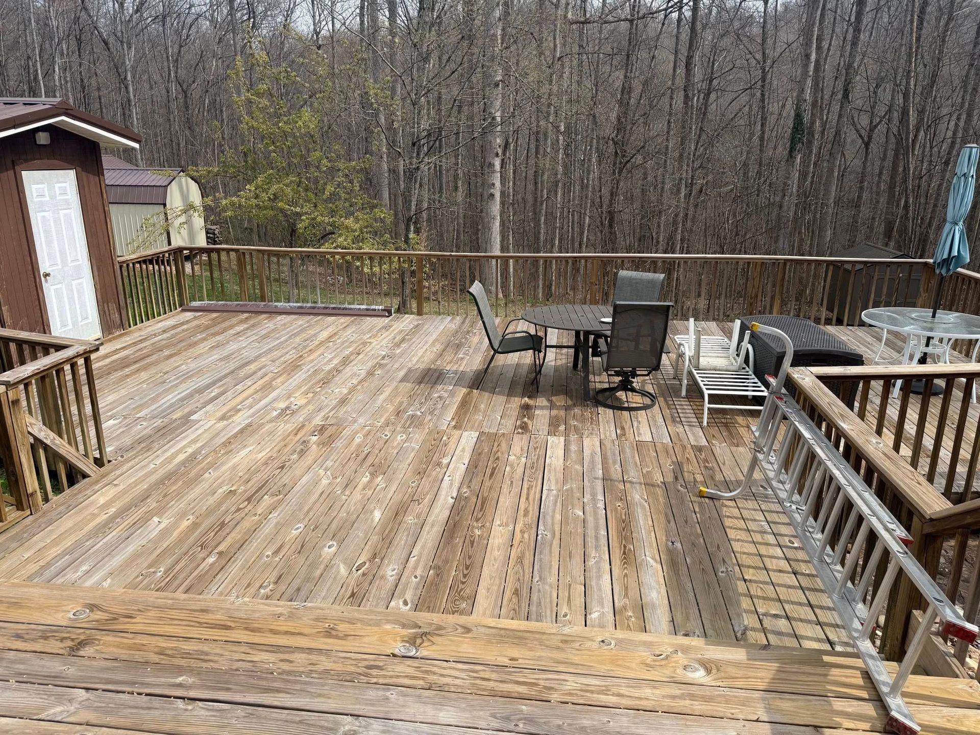 Wooden deck with patio furniture overlooking leafless trees in a wooded backyard