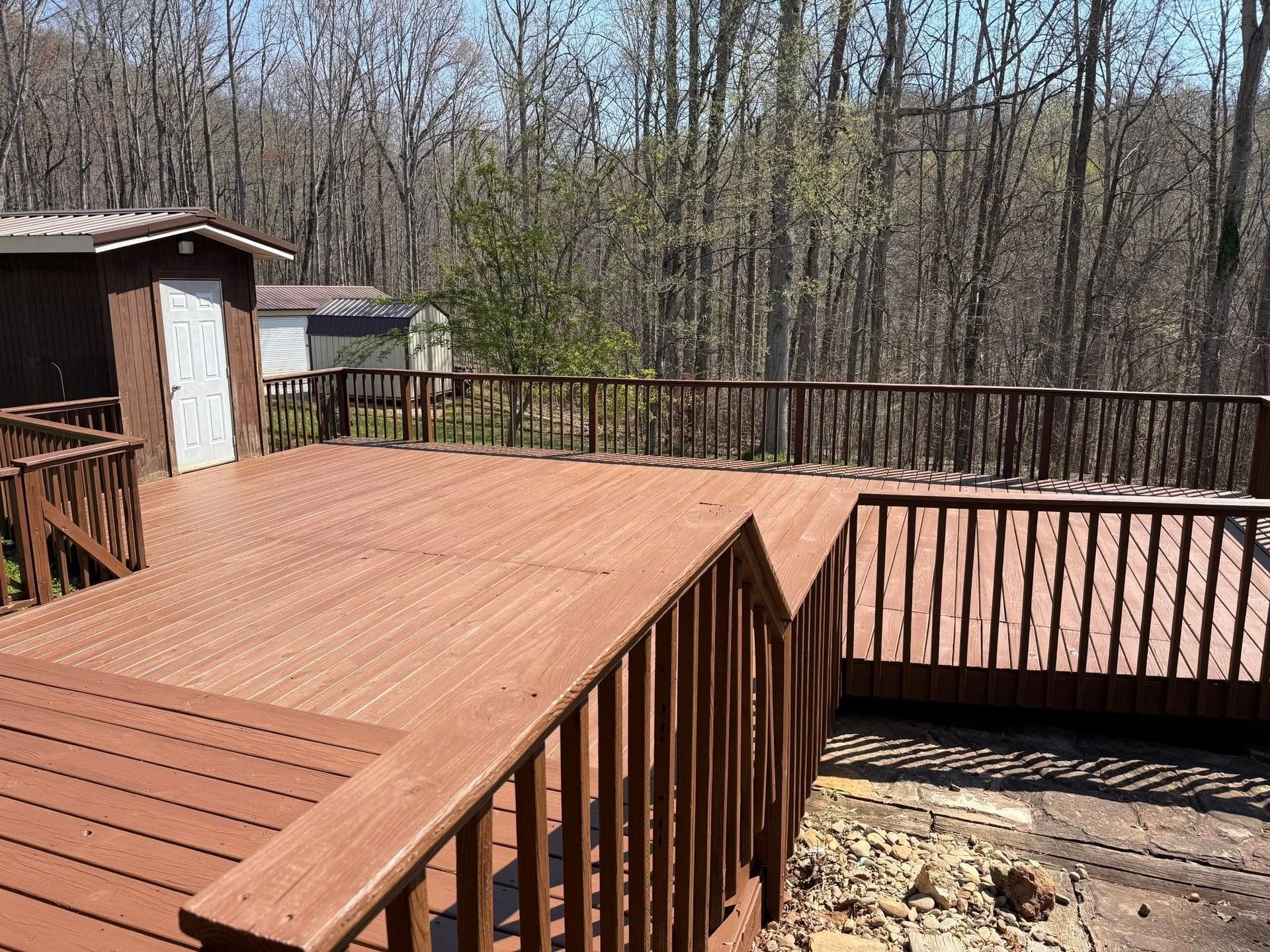 Wooden deck and railing overlooking leafless woods on a sunny day