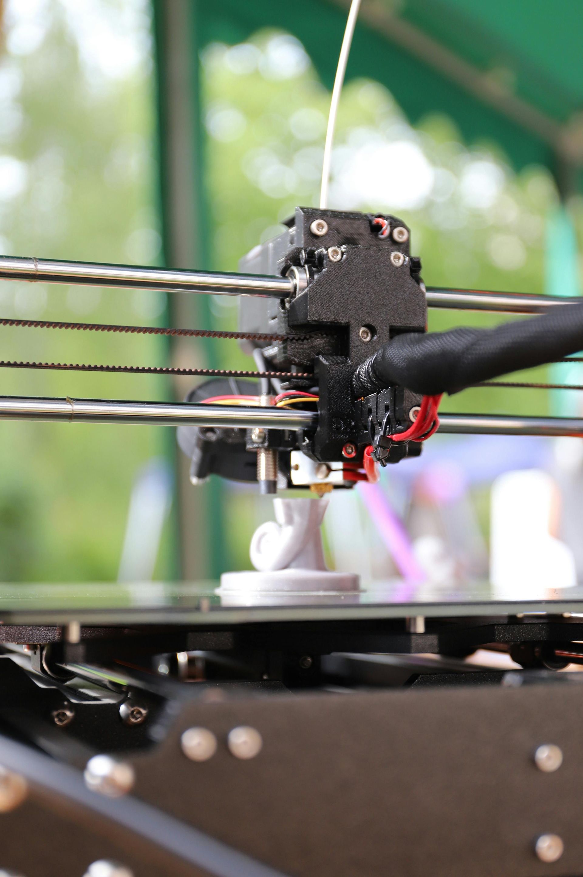 3D printer extruder nozzle printing on a bed, with black frame and wires visible
