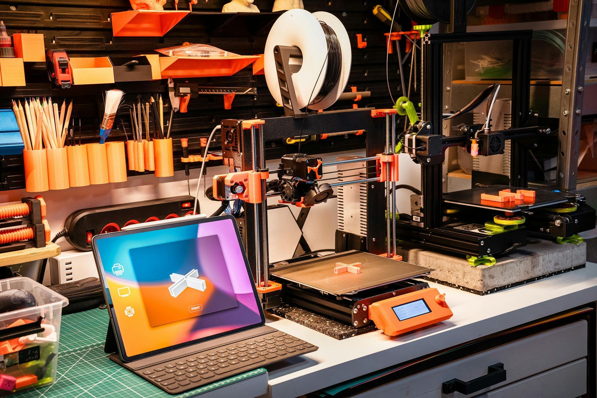 3D printer workshop with laptop, tools, spool holder, and shelves under warm orange lighting
