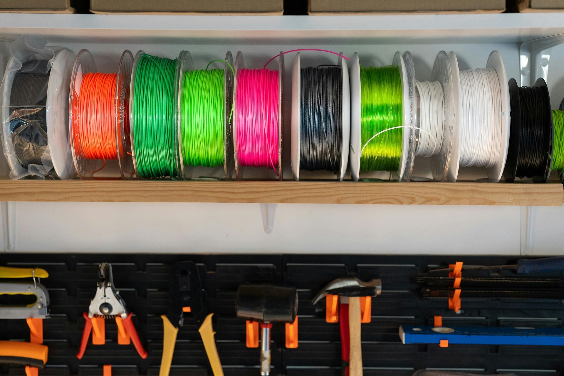 Shelf of coiled colorful wire spools above hanging hand tools in a workshop