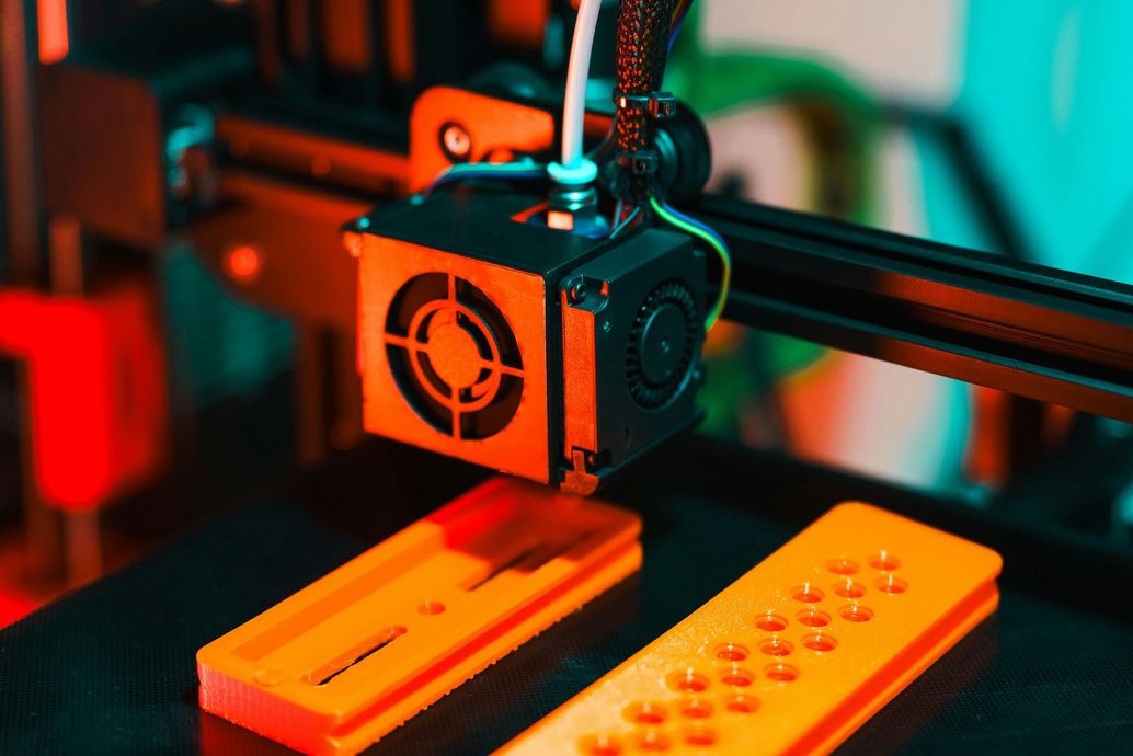 3D printer nozzle extruding orange filament onto a print bed