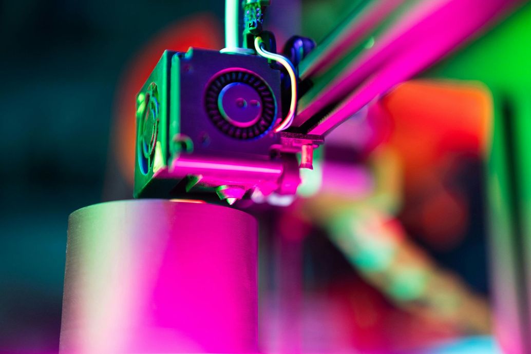 Close-up of a neon-lit 3D printer extruder printing a bright pink object