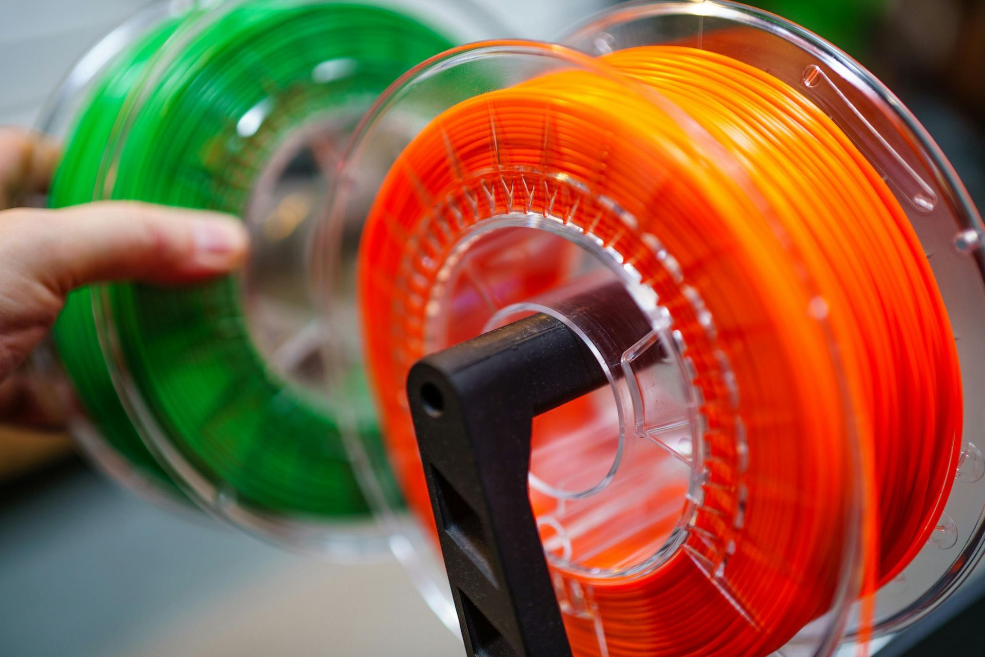 Bright orange and green plastic filament spools on a 3D printer reel holder