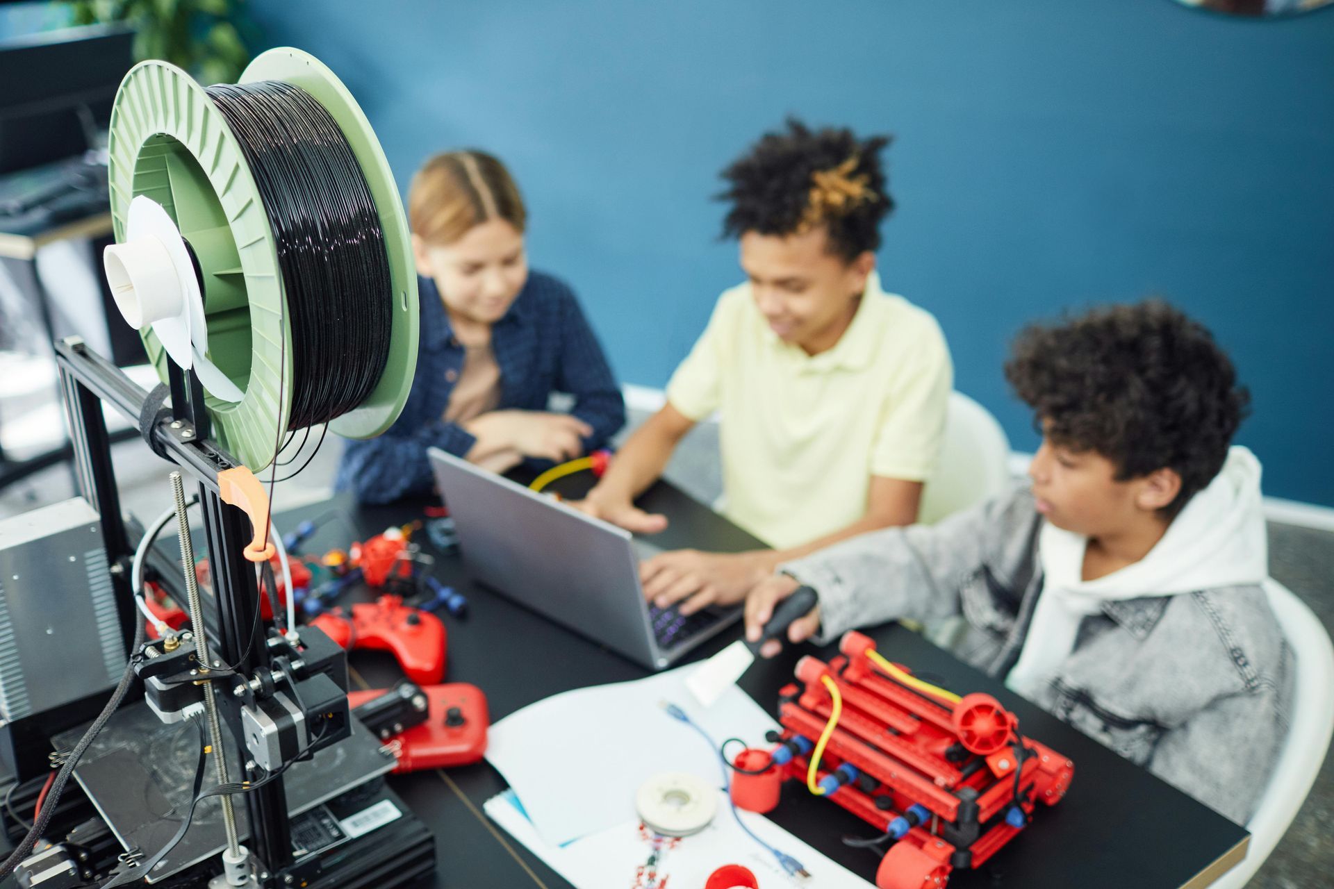 Students using laptops and a 3D printer in a classroom workshop
