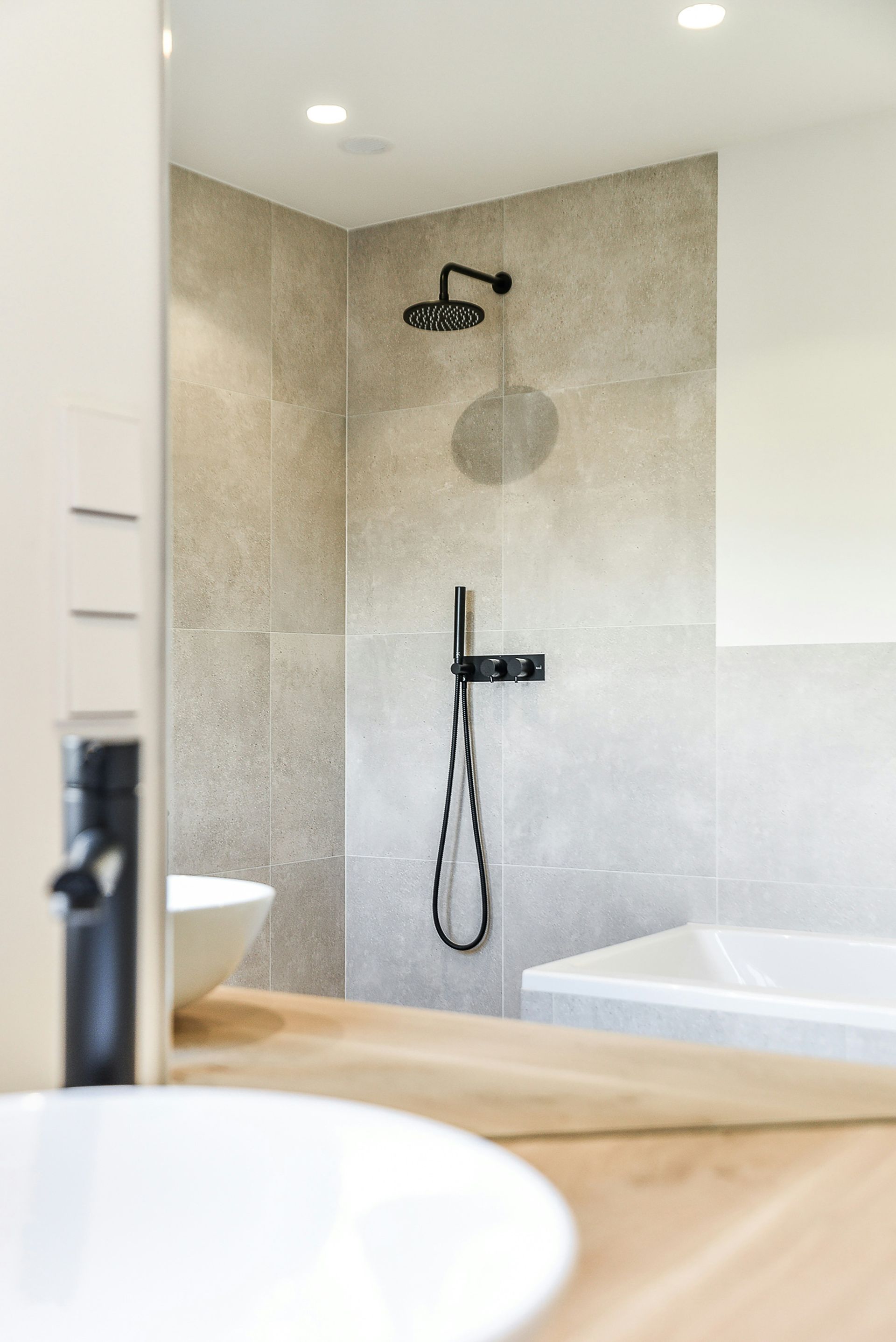 Modern bathroom shower with beige tile, black fixtures, and a bathtub beside it