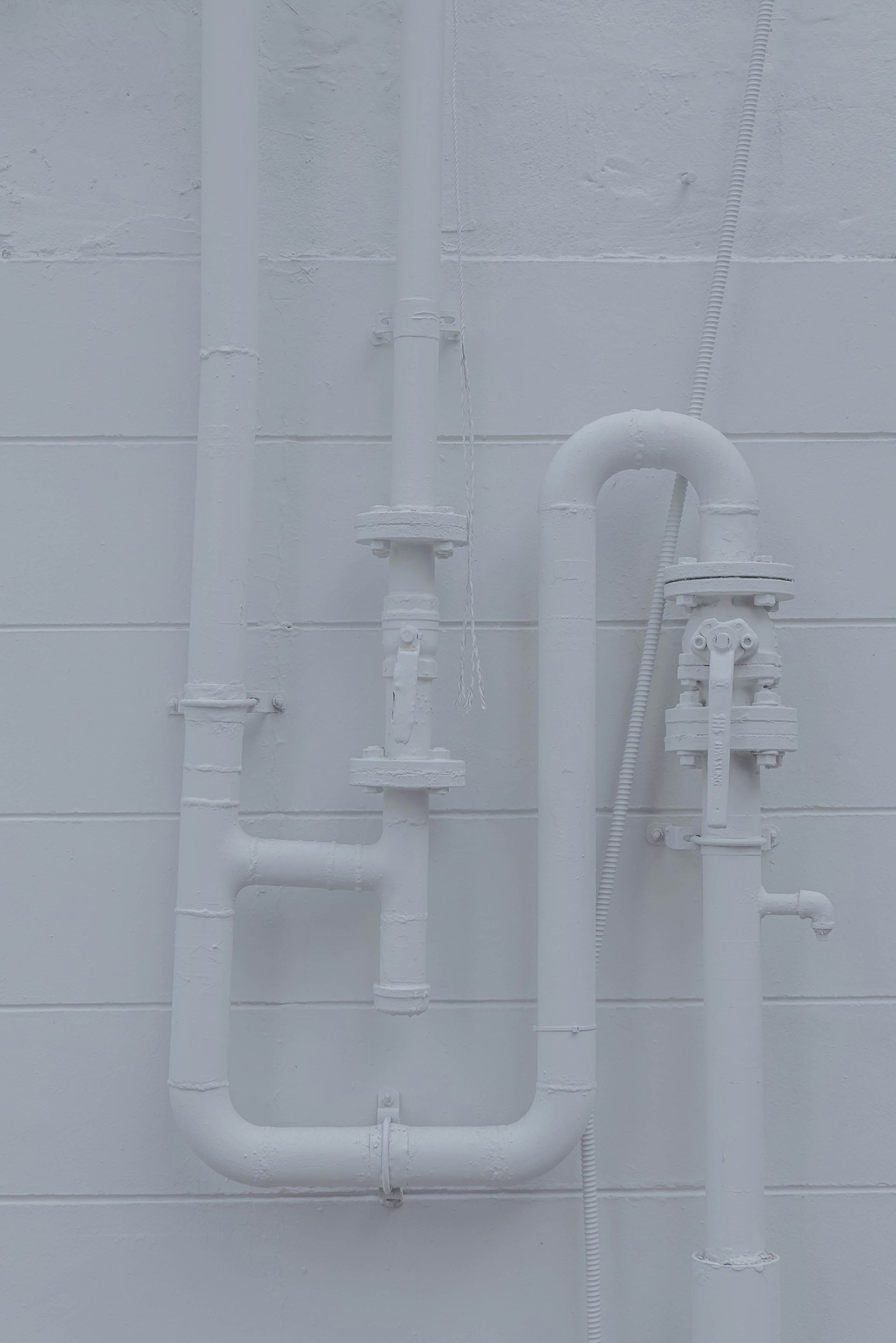White-painted industrial pipes and valves mounted on a tiled wall.