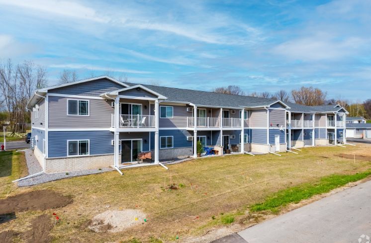 Apartment building with balconies, white siding, and a manicured lawn on a sunny day