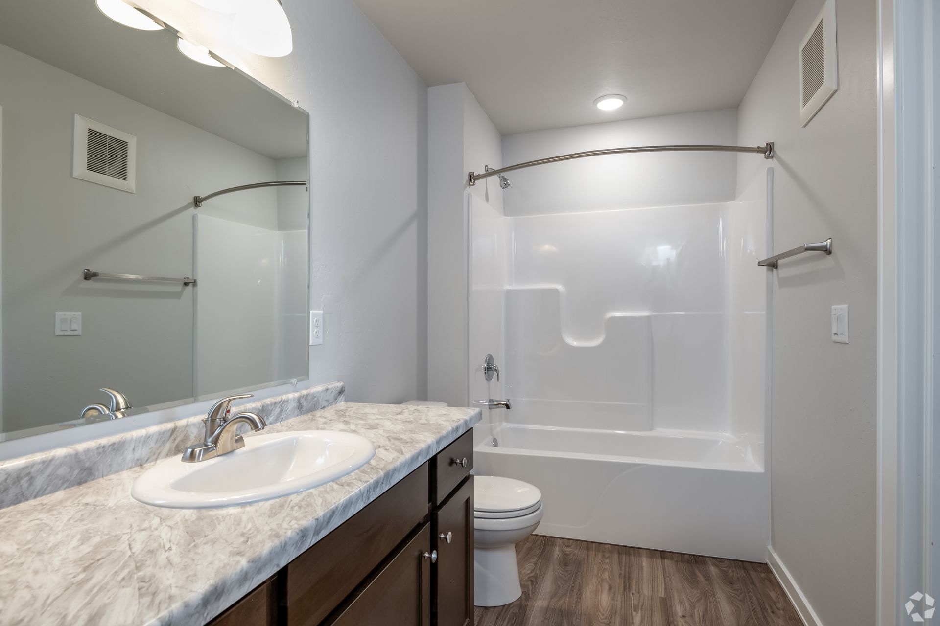 Bathroom with vanity, large mirror, and bathtub-shower combo with curtain rod and wood-look floor.