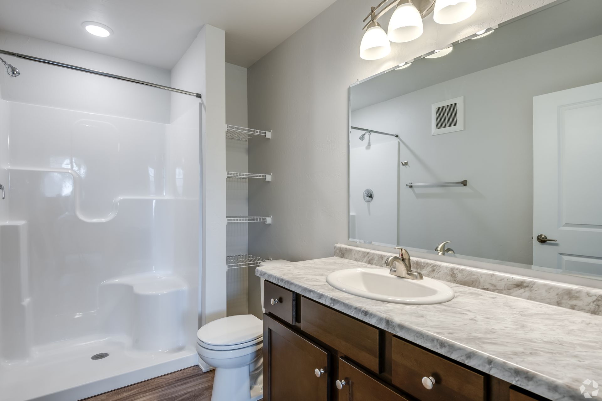Modern bathroom with glass shower, white tub, and granite vanity with mirror lights