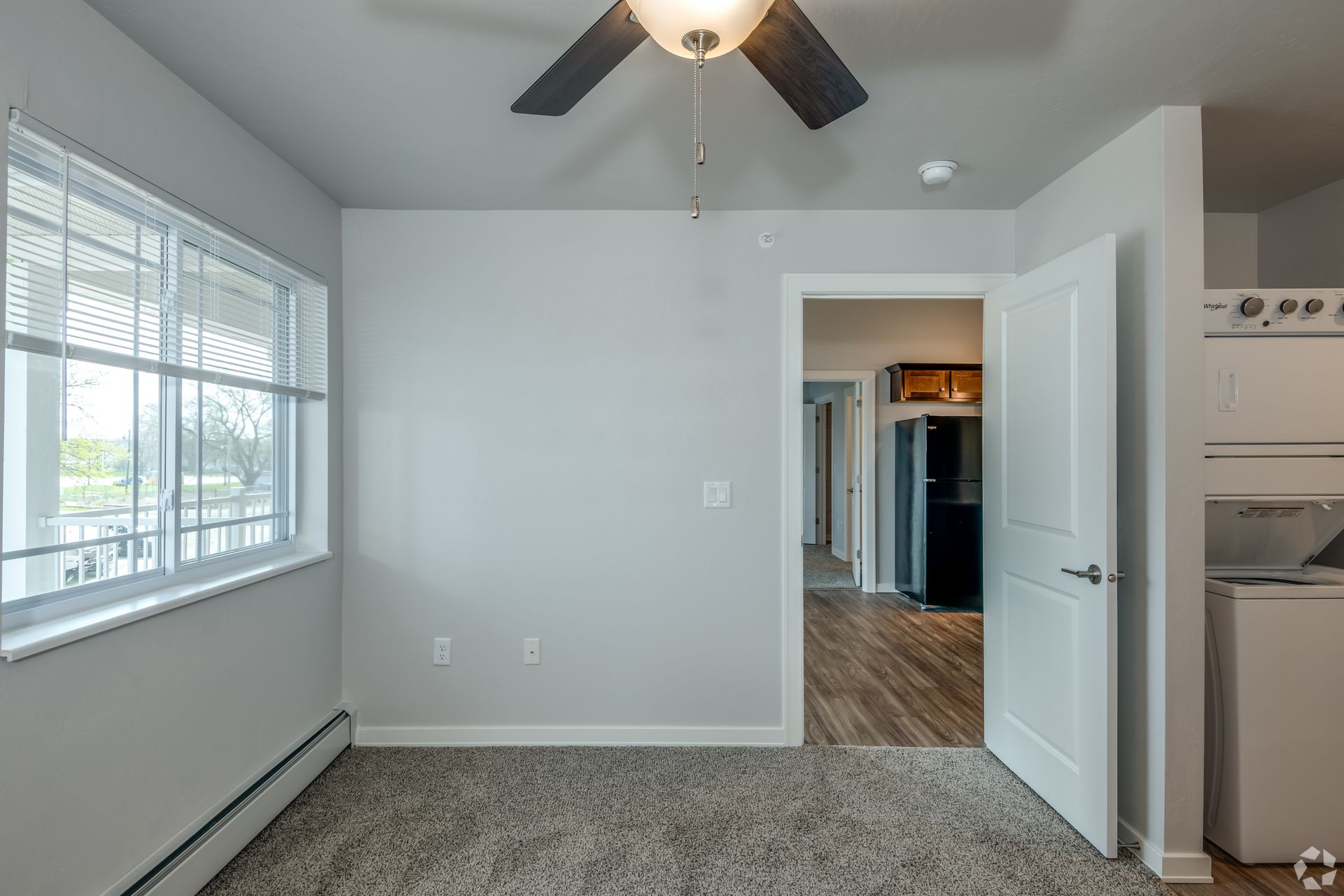 Empty bedroom with carpet, ceiling fan, window blinds, and open door to a closet and hallway.