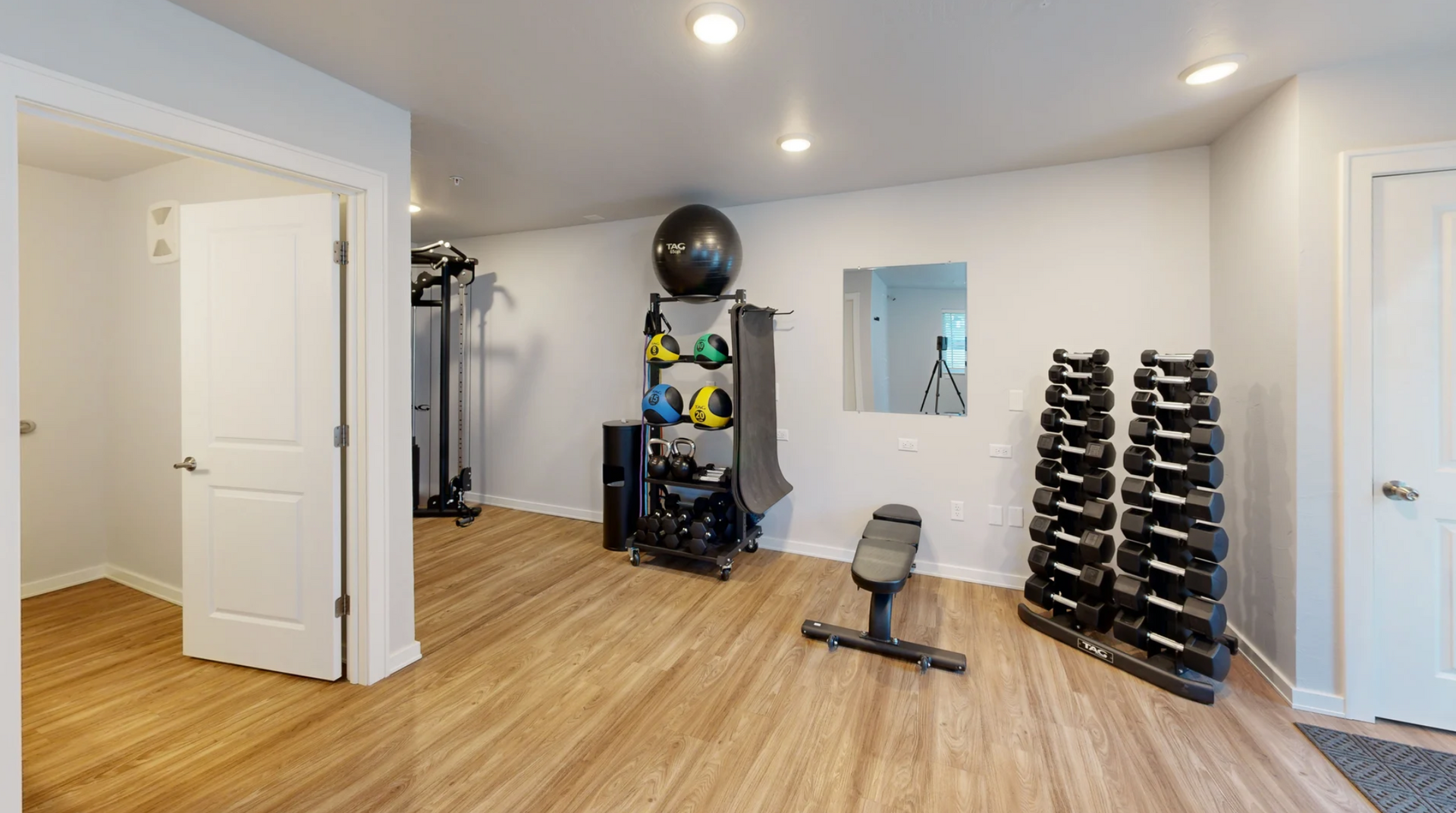 Home gym with hardwood floors, dumbbell rack, bench, exercise equipment, and wall mirror