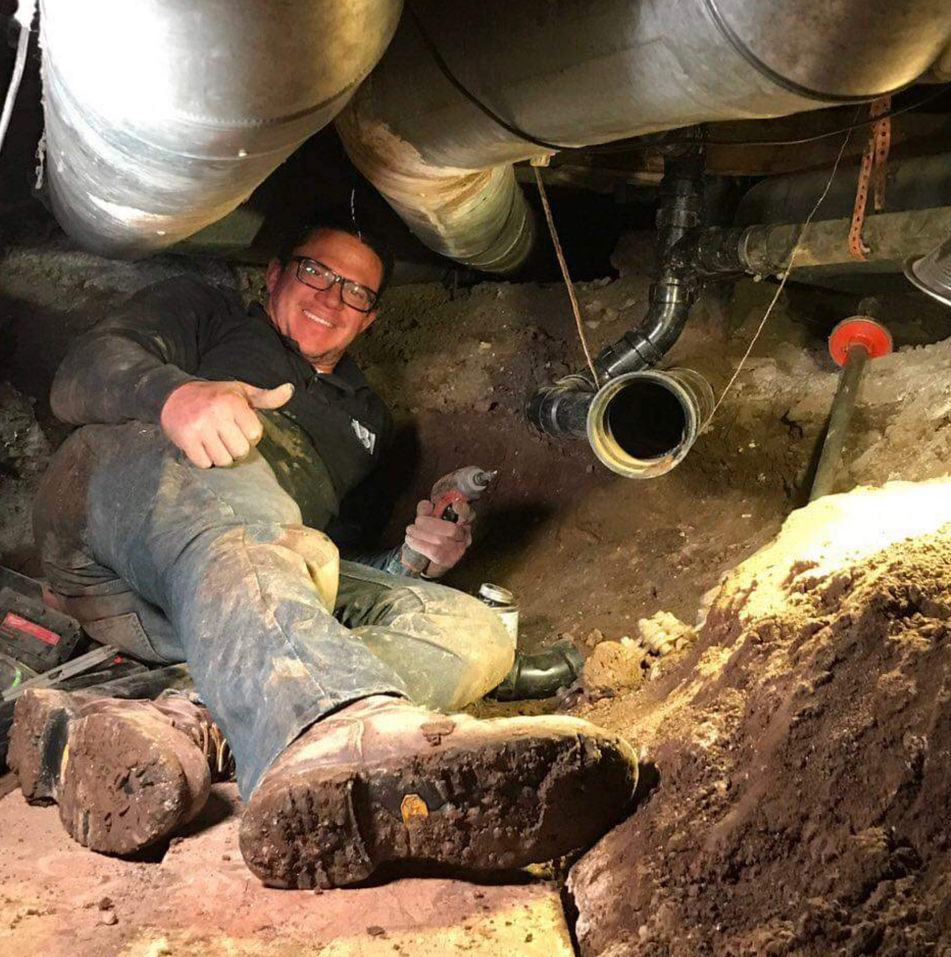 A man is laying in the dirt under a pipe