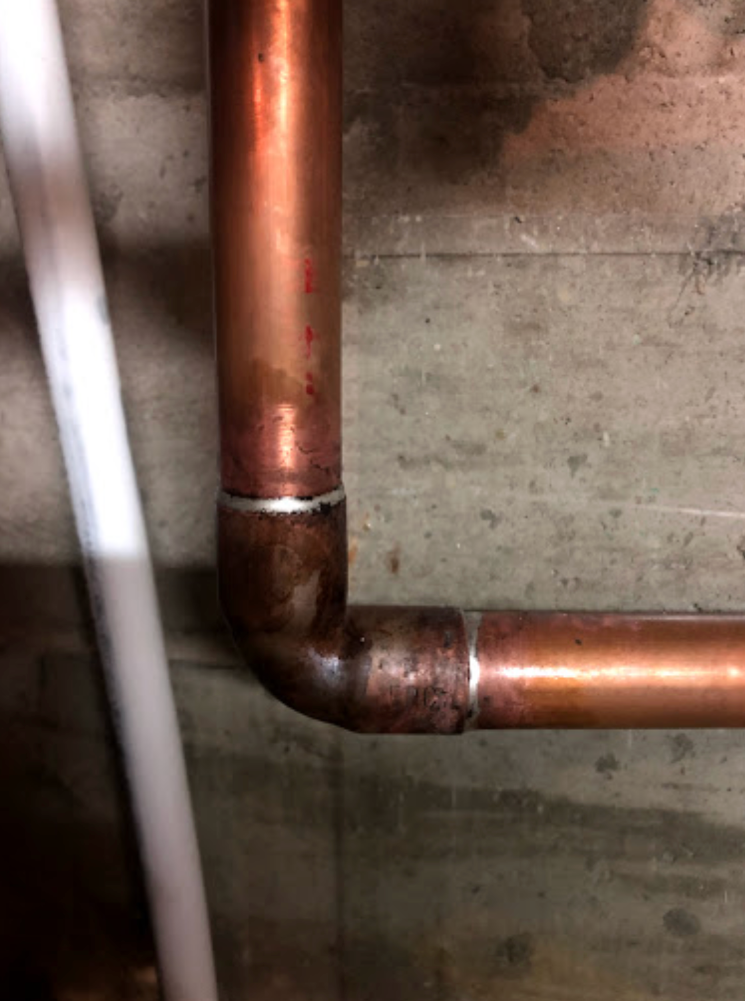 A close up of a copper pipe against a concrete wall.