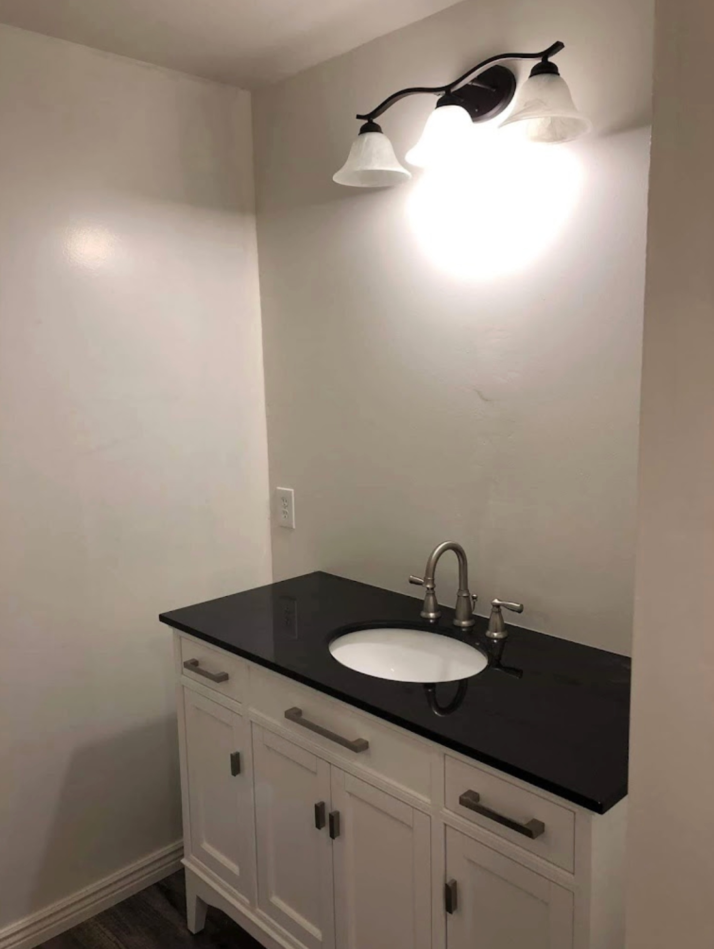 A bathroom vanity with a black counter top and a sink.