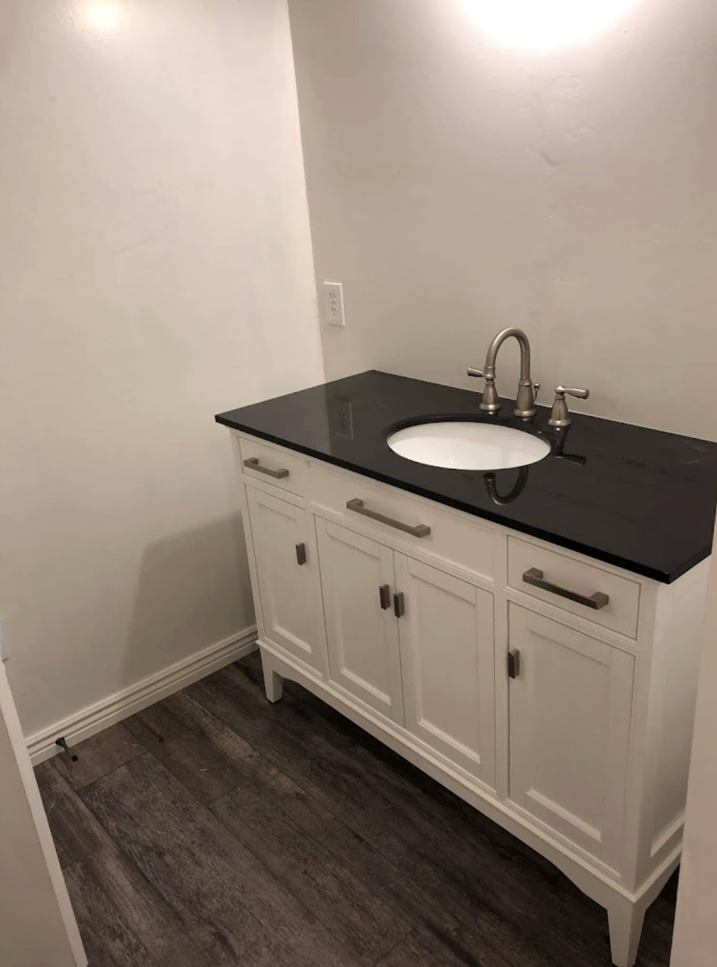 A bathroom vanity with a black counter top and a sink.