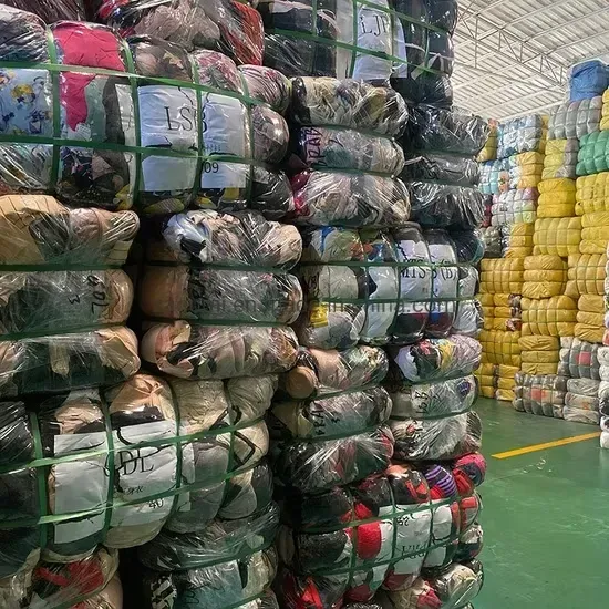 Montones de ropa o textiles empaquetados y envueltos en plástico en un pasillo de un almacén.