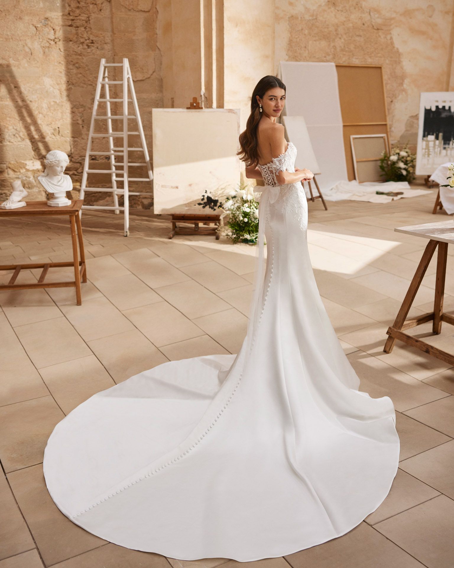 Sposa in abito bianco a sirena con lungo strascico in posa in uno studio d'arte.