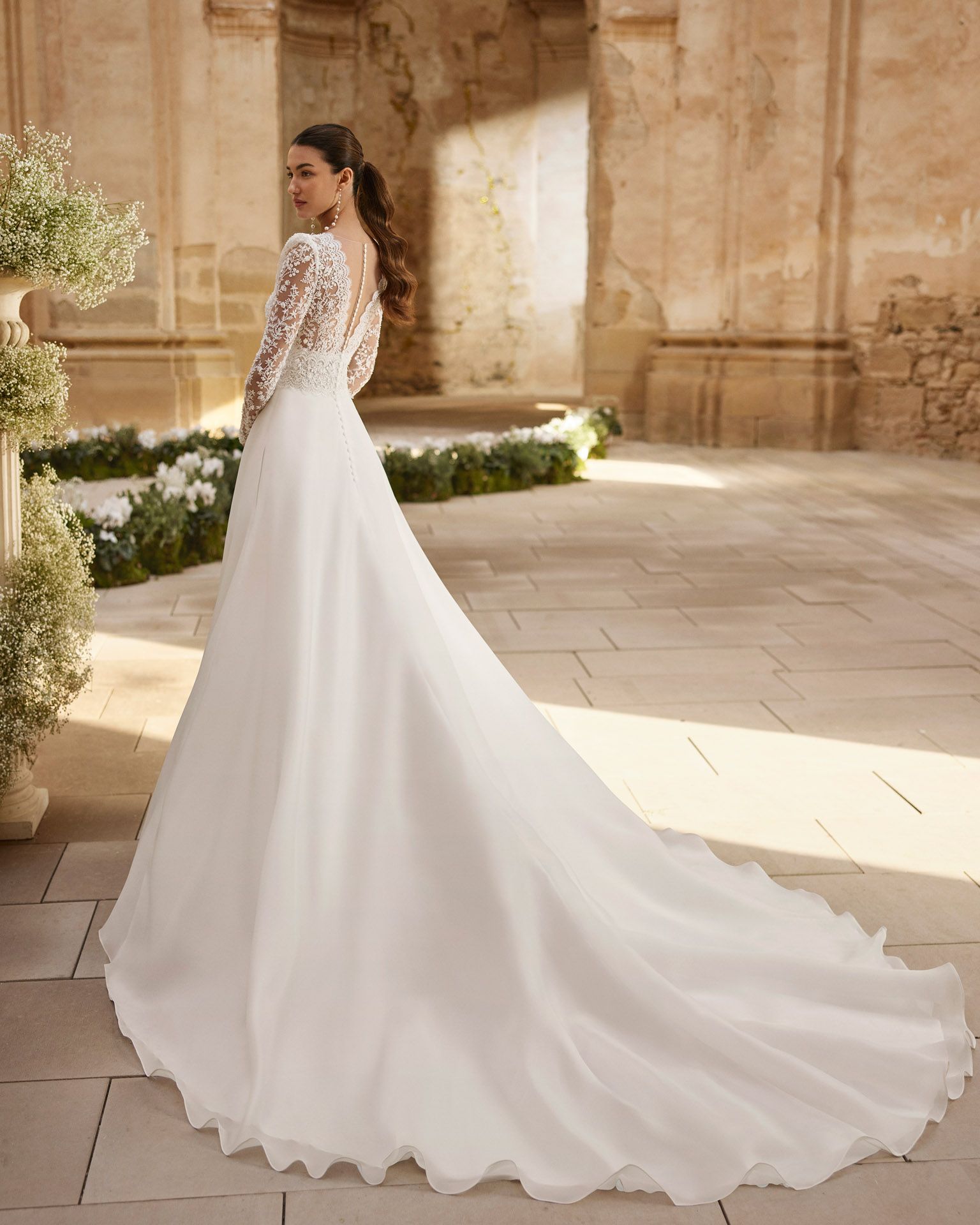 Sposa in abito da sposa bianco con lungo strascico in una chiesa illuminata dal sole.