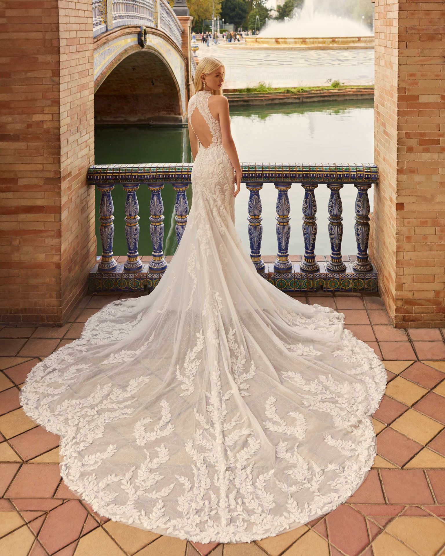 Donna in abito da sposa con lungo strascico su un balcone con vista su una fontana.