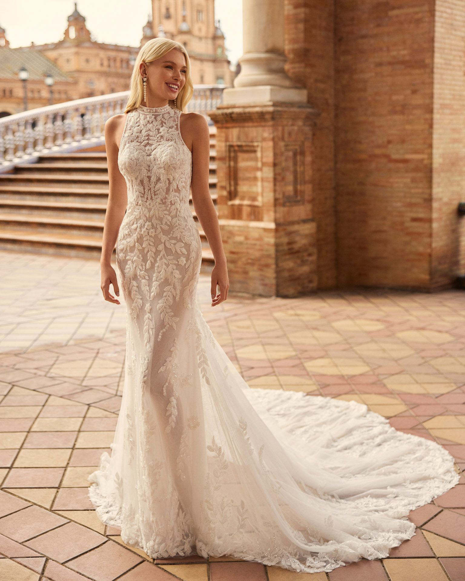 Donna sorridente in abito da sposa in pizzo bianco con strascico, all'aperto.