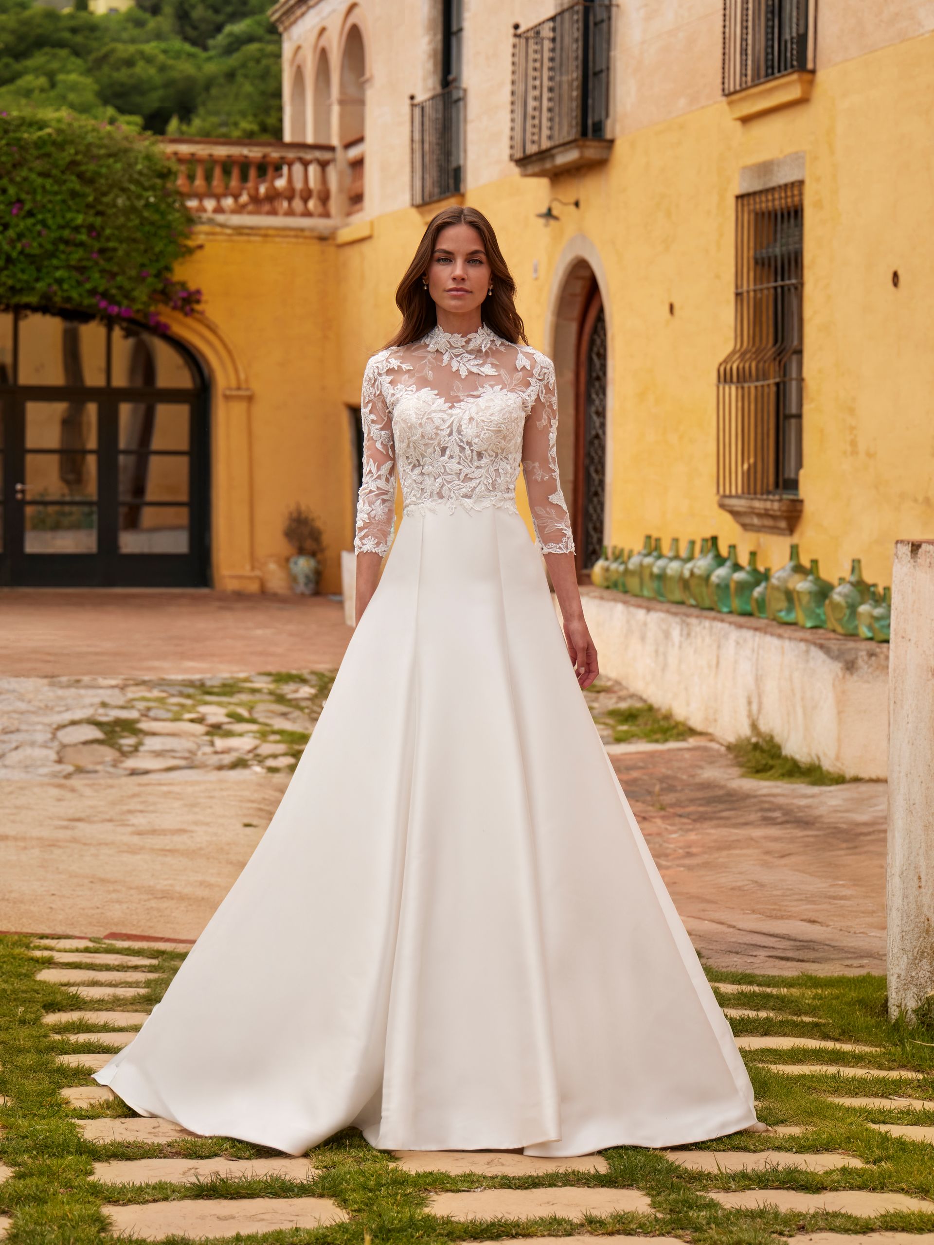 Una donna in abito da sposa bianco è in piedi all'esterno; sullo sfondo si vede un edificio giallo.