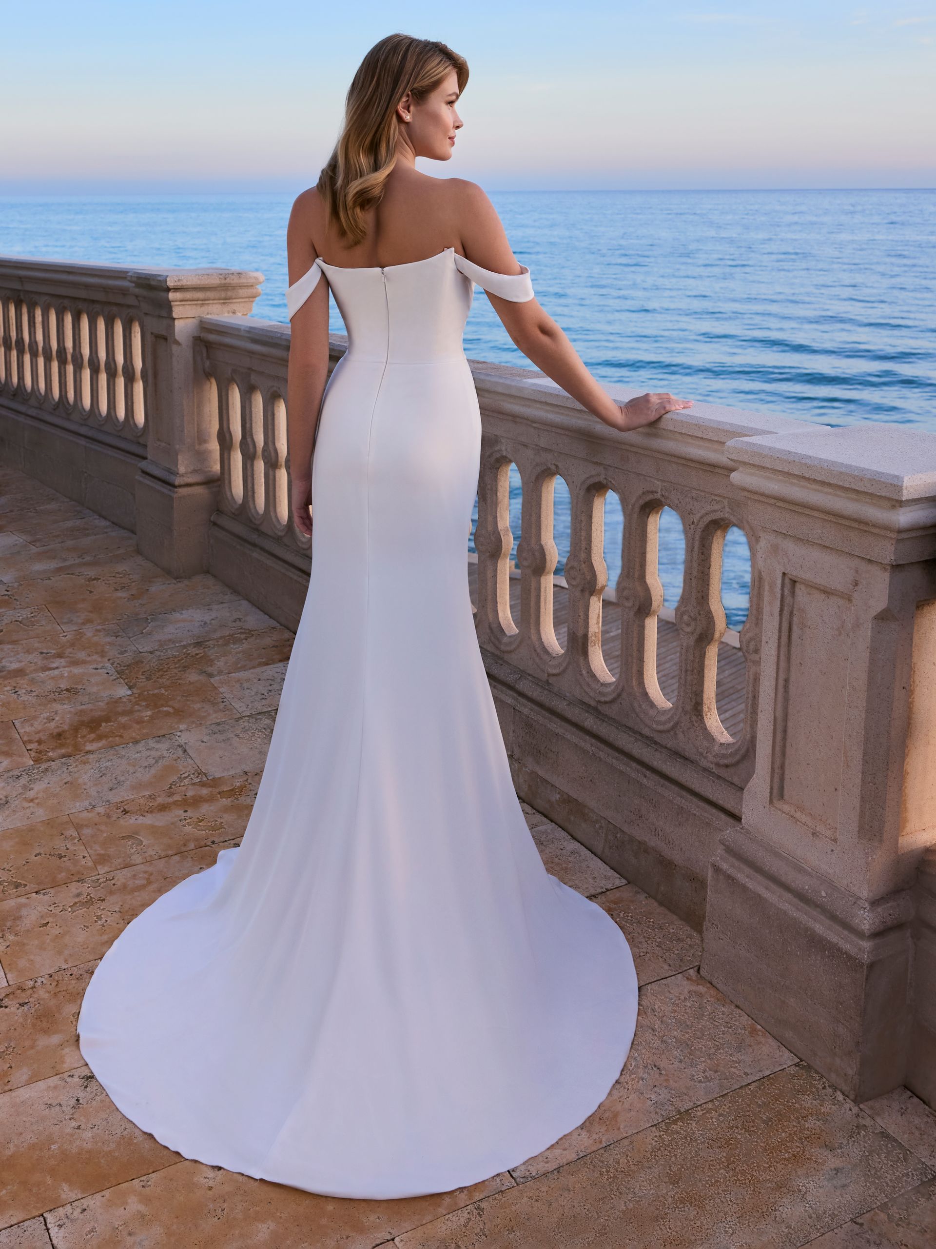 Donna in abito da sposa bianco, vista oceano, appoggiata alla ringhiera.
