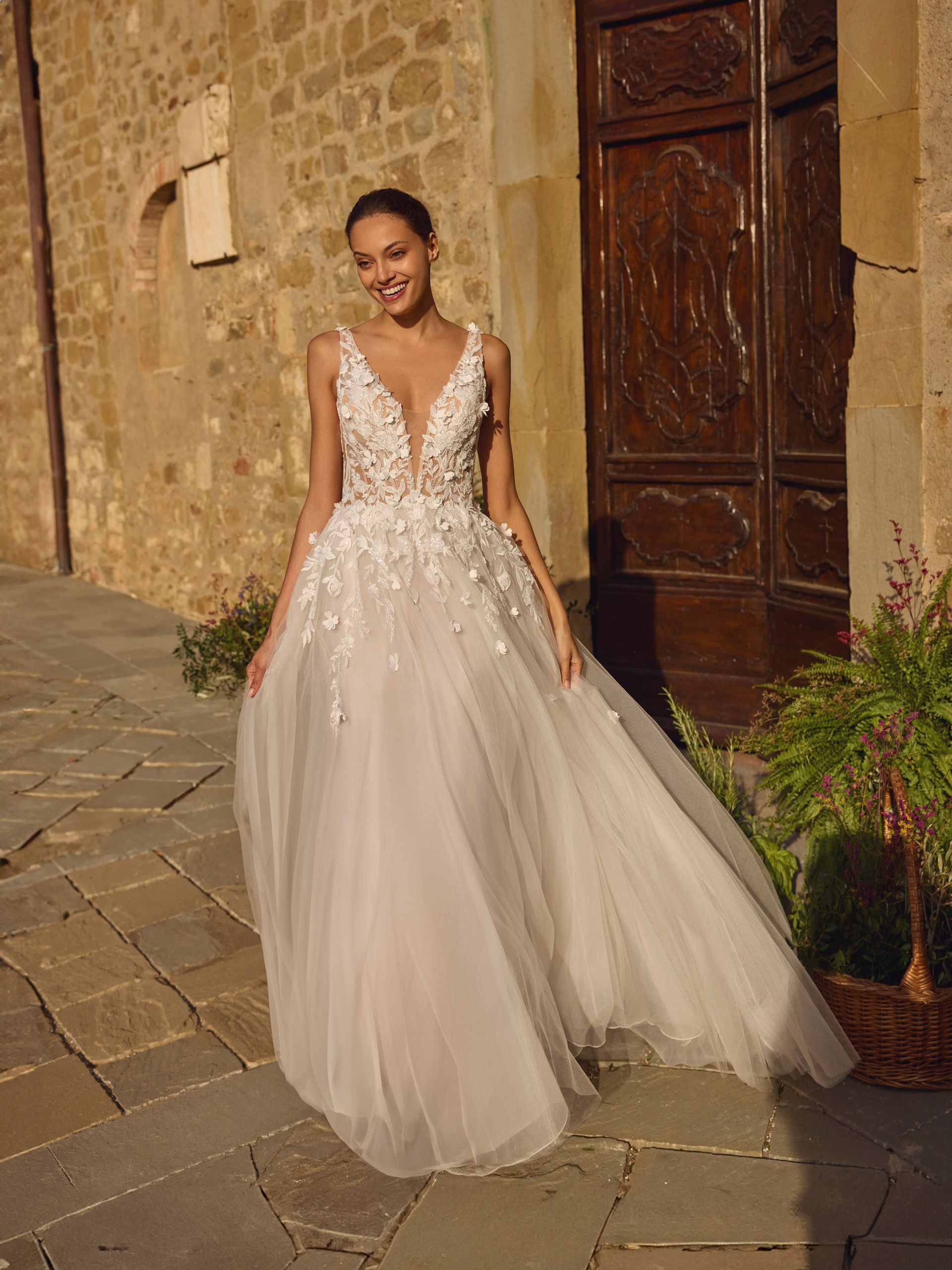 Una donna in abito da sposa bianco sorride fuori da un edificio in pietra.