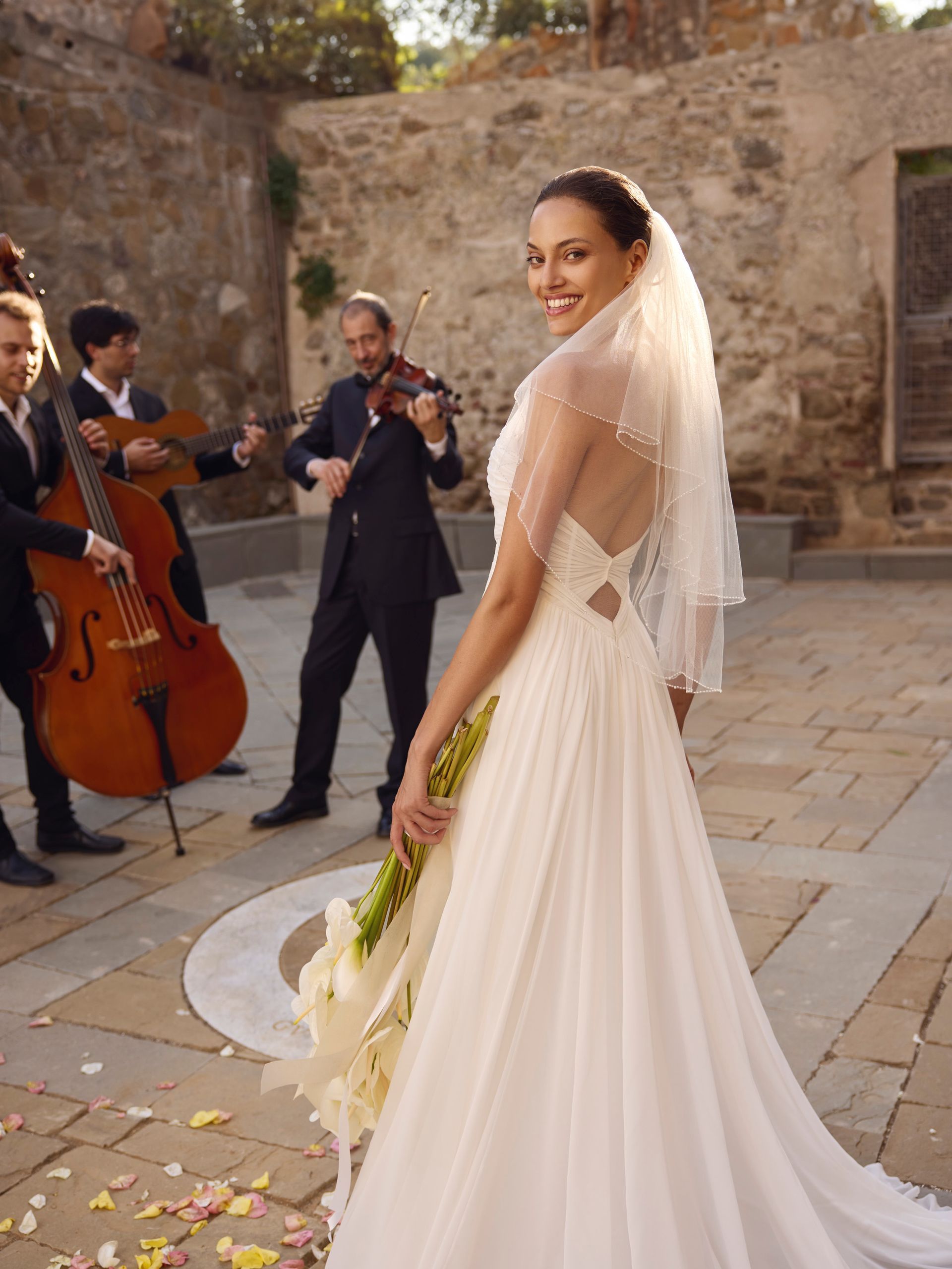 Sposa in abito da sposa con musicisti all'aperto, sorridente.