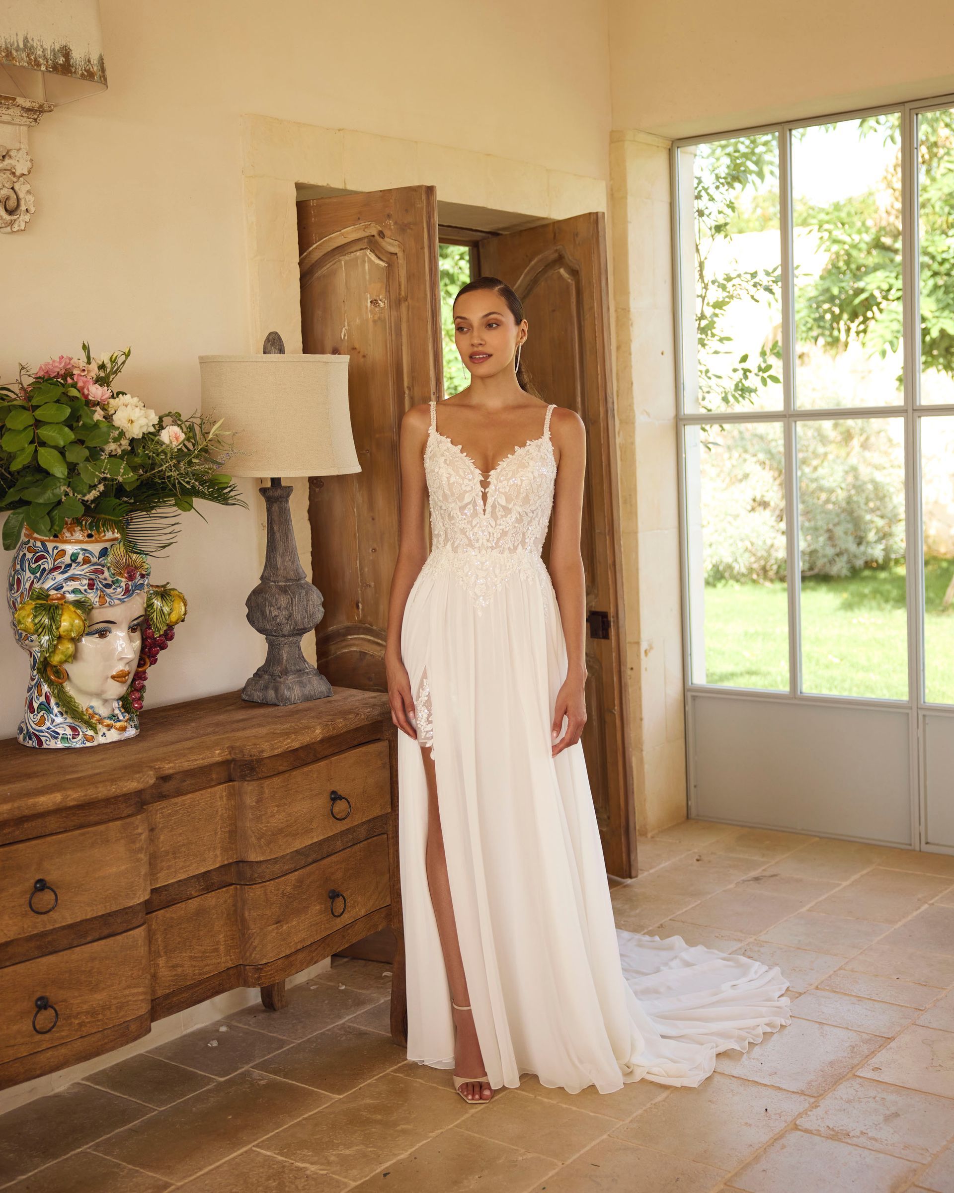 Una donna in abito da sposa è in piedi sulla soglia di una porta con uno spacco profondo.