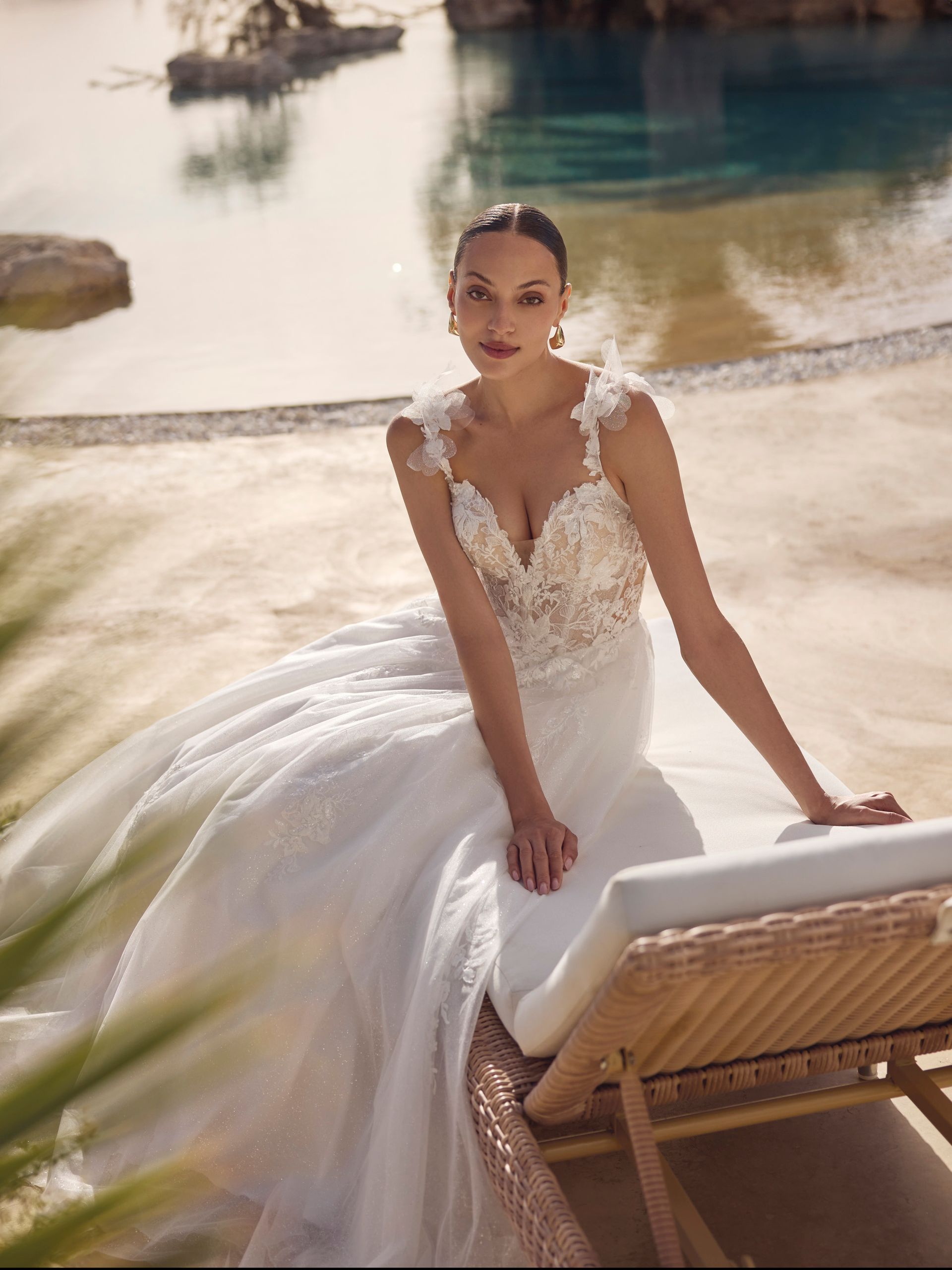Una donna in abito da sposa bianco è seduta su una sedia a sdraio vicino all'acqua.