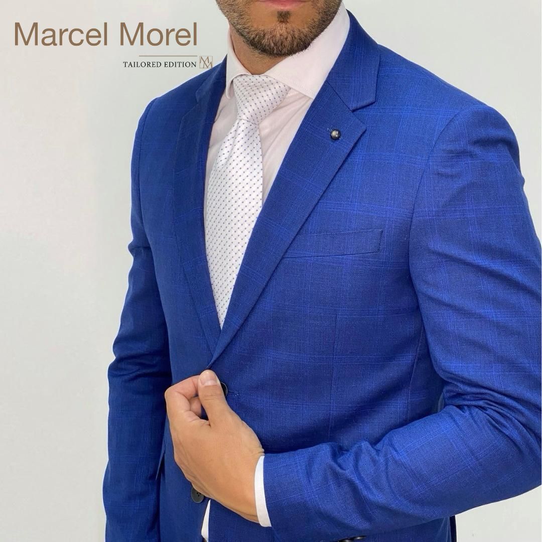 Uomo in abito blu, camicia rosa e cravatta bianca, mano sulla giacca.