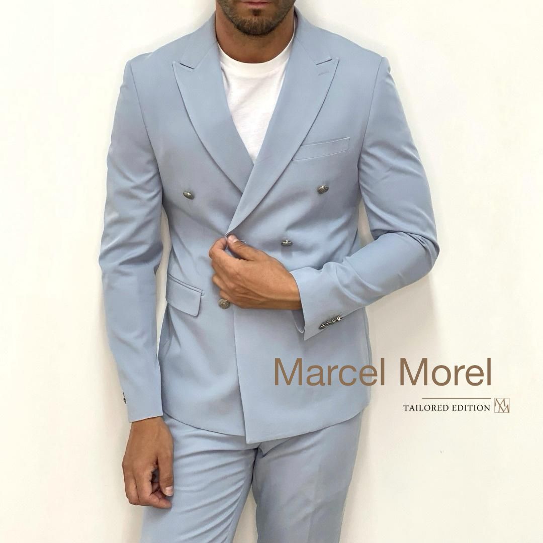 Uomo in abito doppiopetto azzurro e maglietta bianca, in posa. Logo di Marcel Morel.
