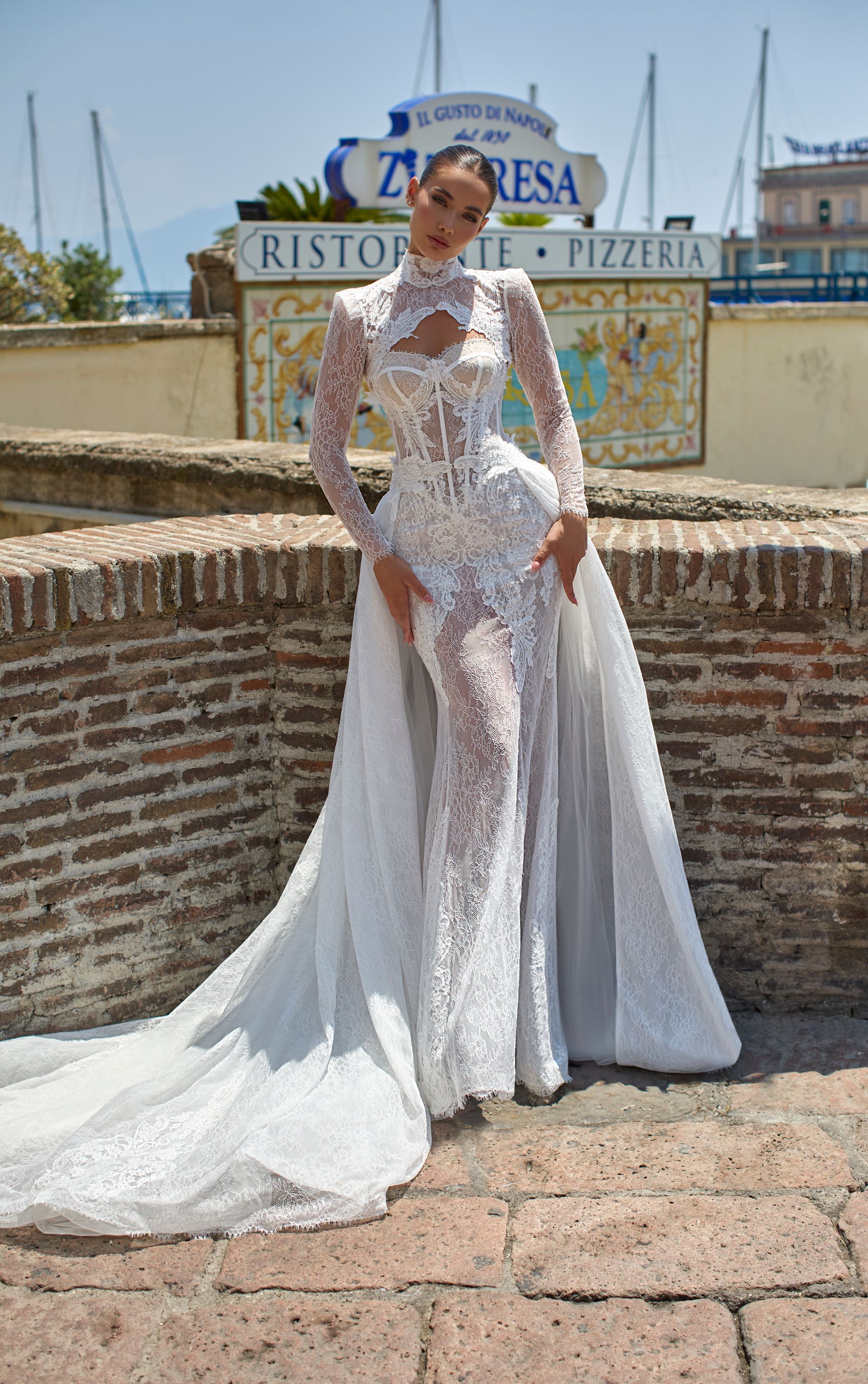 Donna in abito bianco decorato con gioielli e lungo strascico, in posa fuori da un ristorante.
