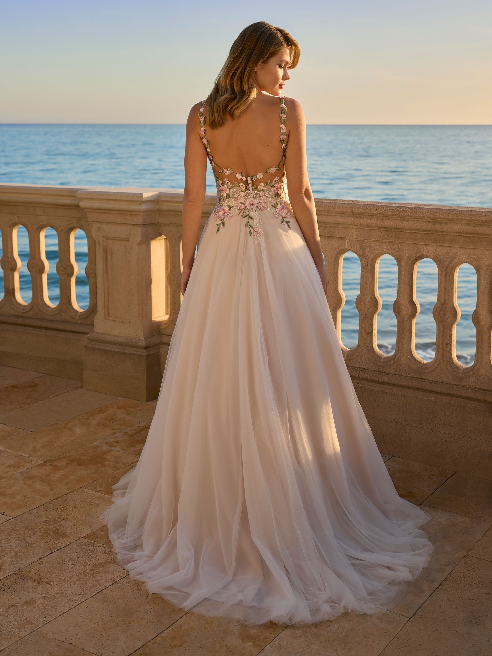Donna in abito da sposa con corpetto floreale, in piedi sul balcone con vista sull'oceano.