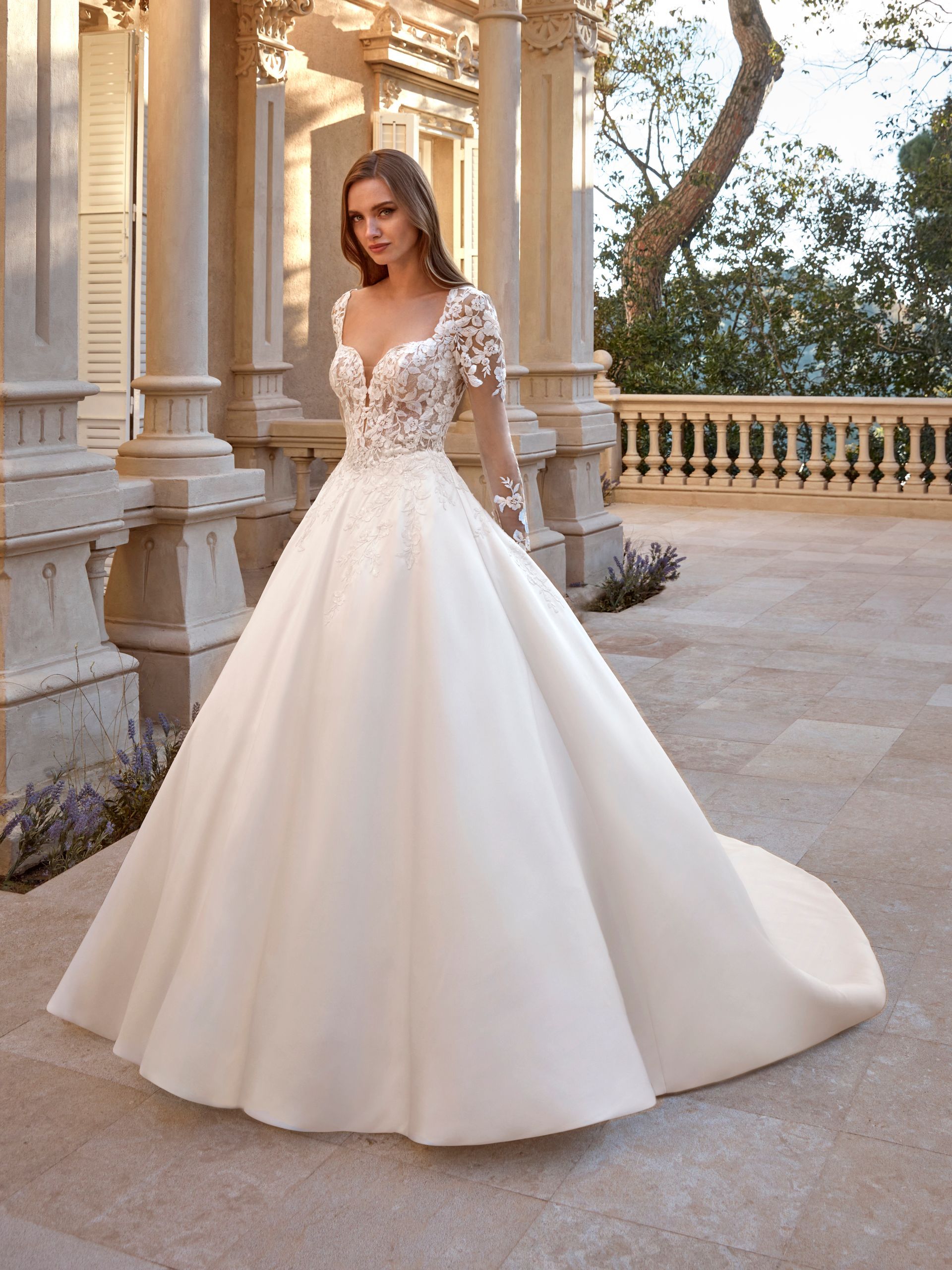 Donna in abito da sposa bianco con corpetto in pizzo, in posa all'aperto davanti alle colonne.