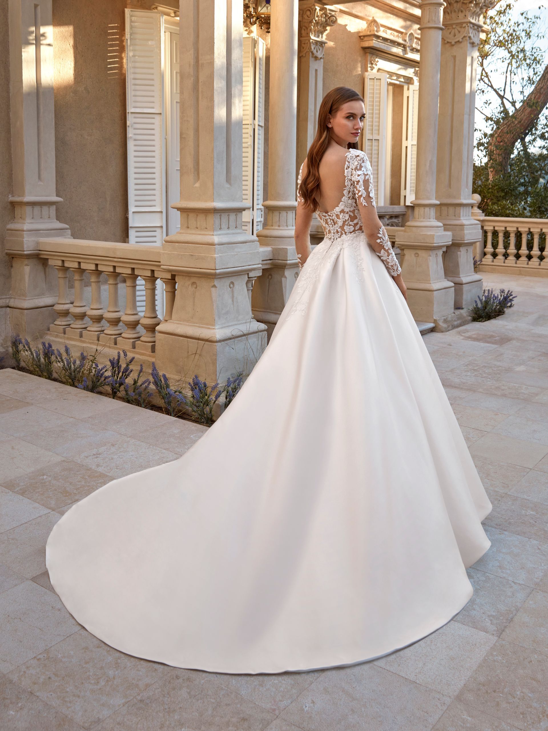 Una donna in abito da sposa bianco con lungo strascico posa all'aperto vicino alle colonne.