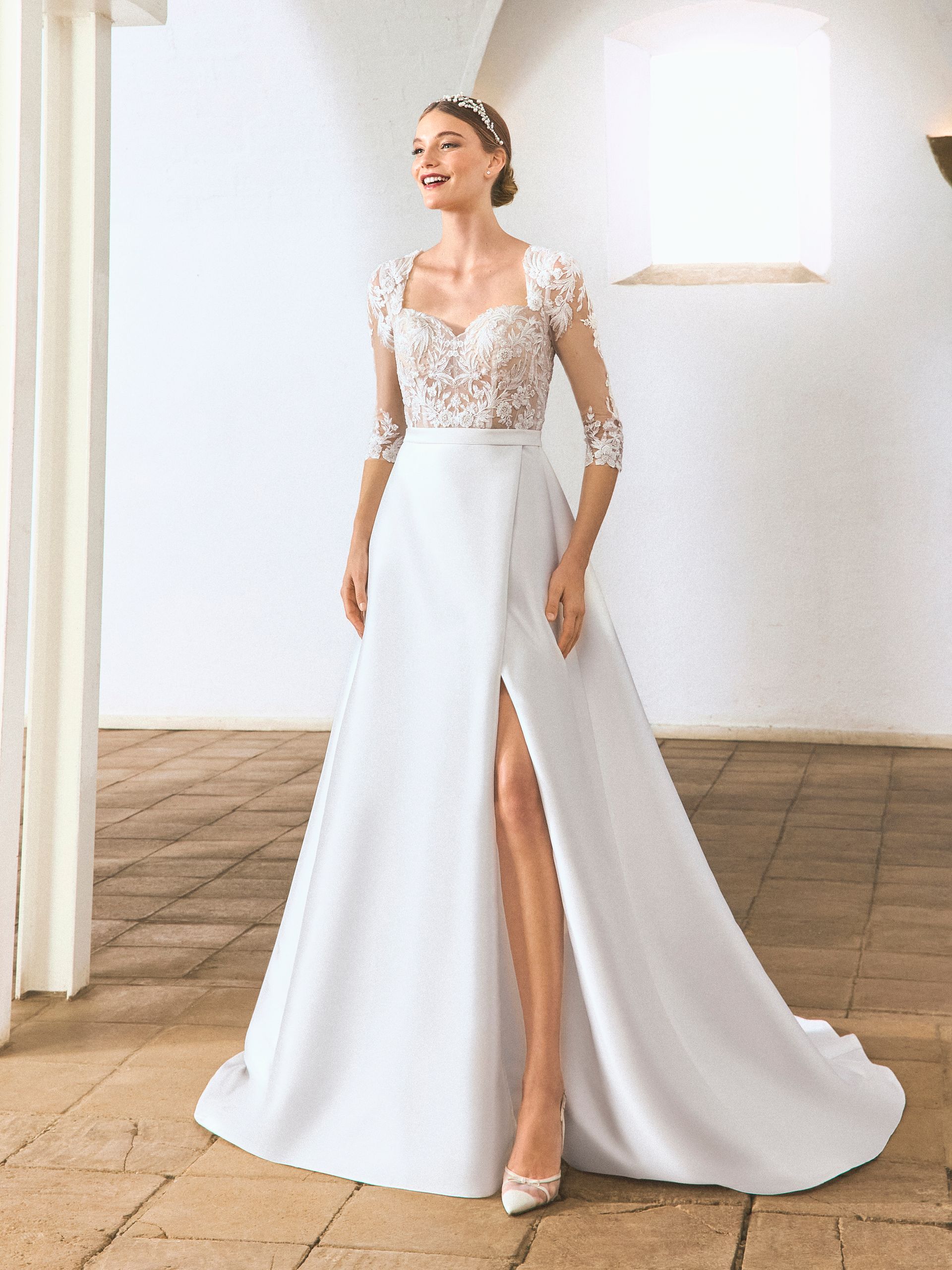 Donna sorridente in abito da sposa bianco con corpetto in pizzo e spacco profondo.