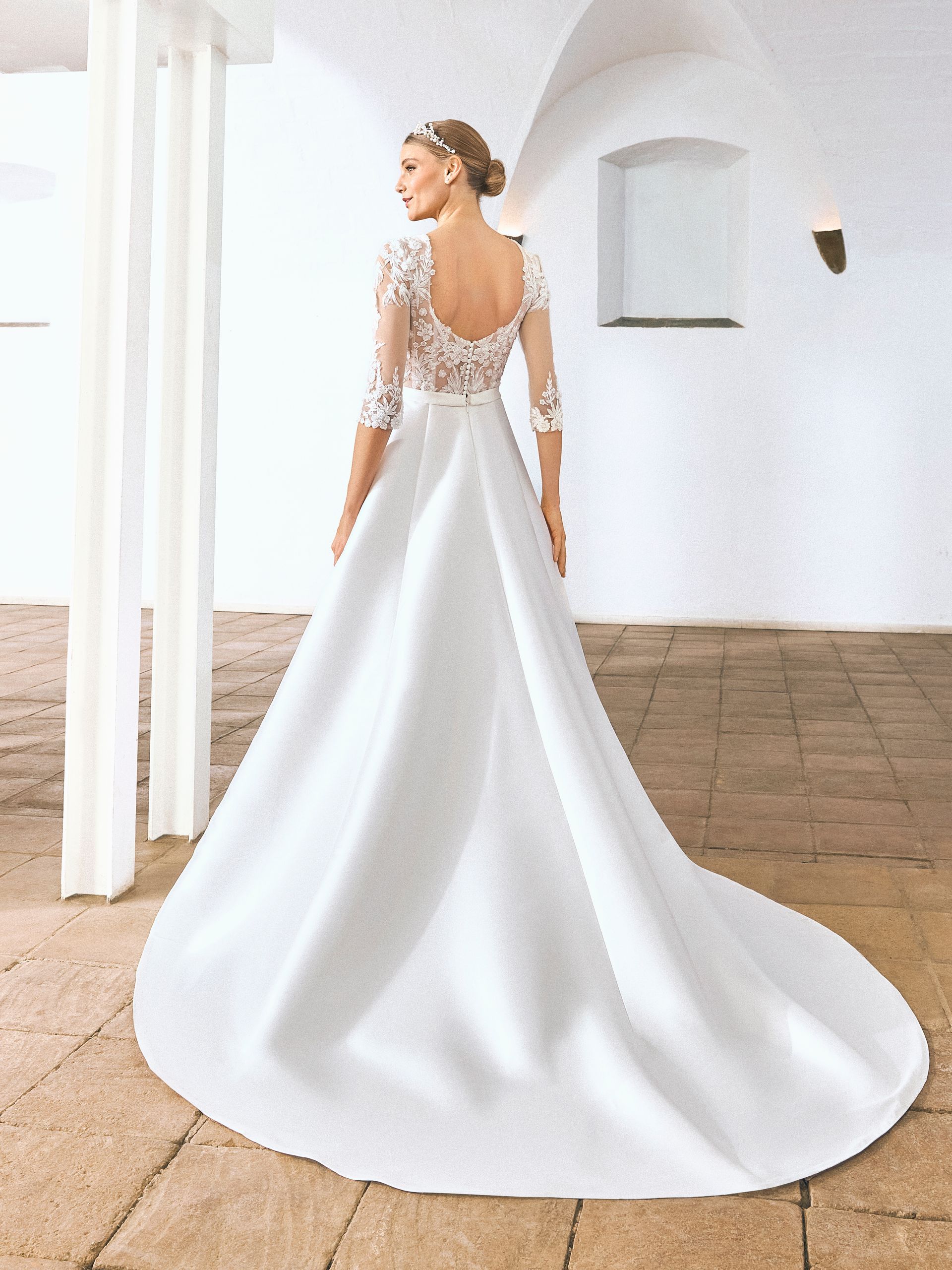 Donna in abito da sposa bianco, vista posteriore, maniche in pizzo, lungo strascico.