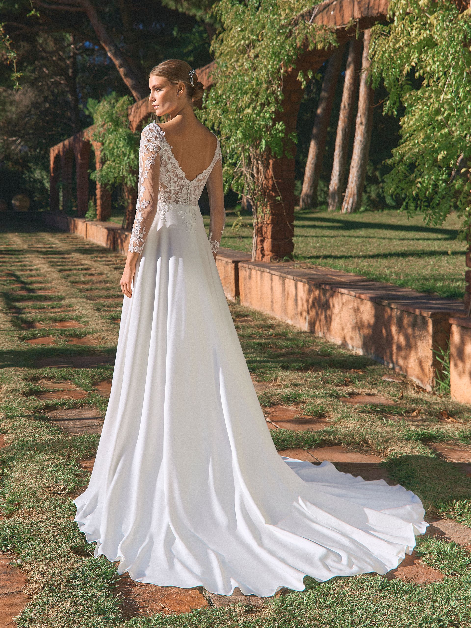 Sposa in abito da sposa bianco con lungo strascico, all'aperto, in un ambiente soleggiato.