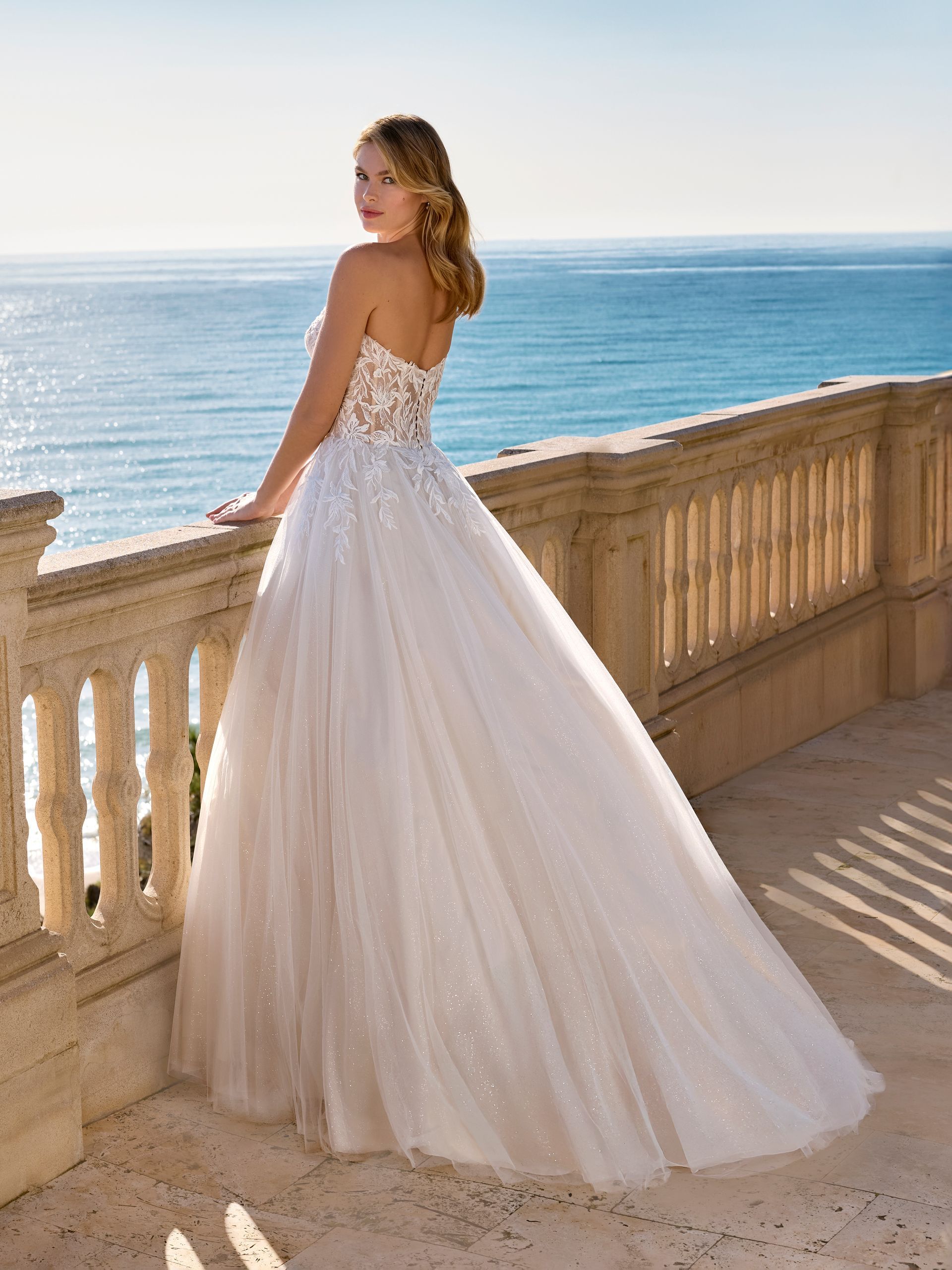 Donna in abito da sposa senza spalline su un balcone con vista sull'oceano.