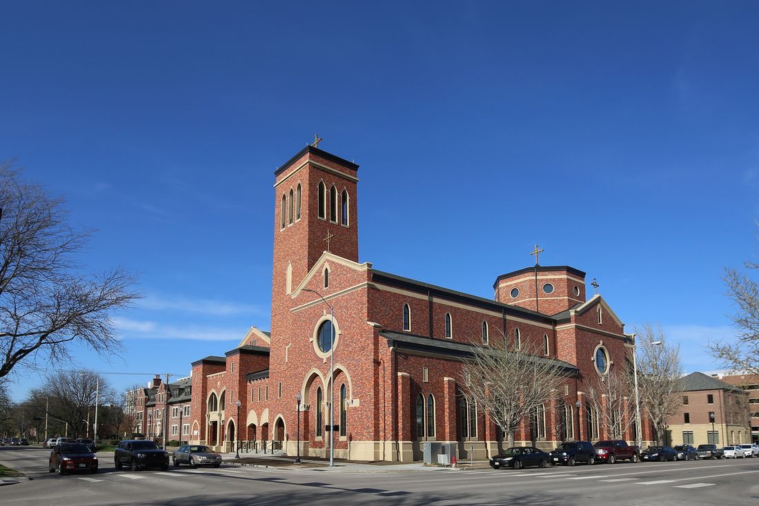 A large red brick church with cars parked in front of it on a sunny day.