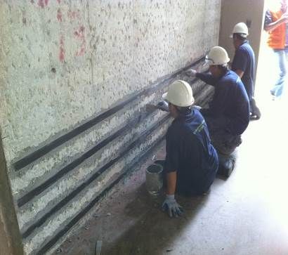 Obreros con cascos instalan tuberías a lo largo de una pared en un estrecho pasillo de construcción.